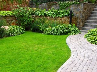 A brick walkway leading to a lush green lawn and stairs.