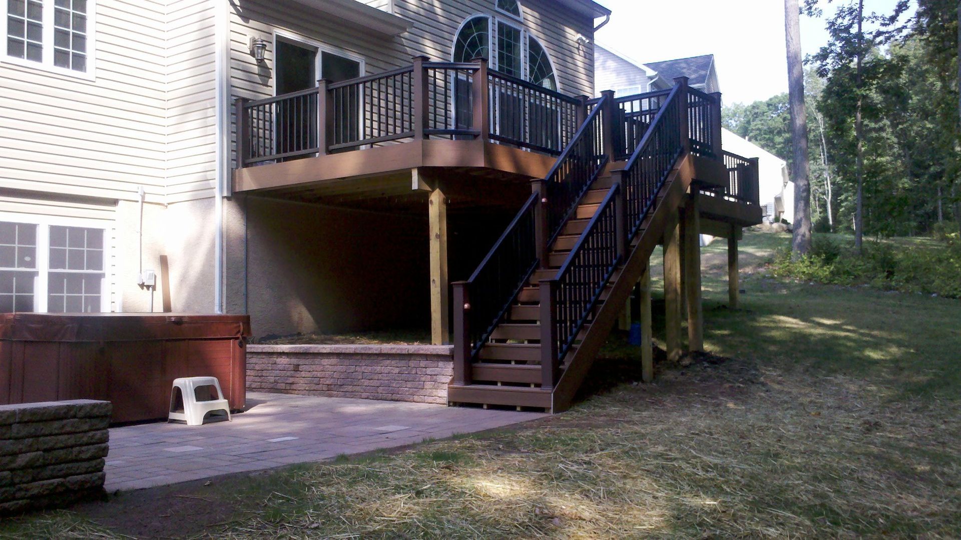 Backyard with a raised wooden deck, stairs, hot tub, and stone retaining wall.