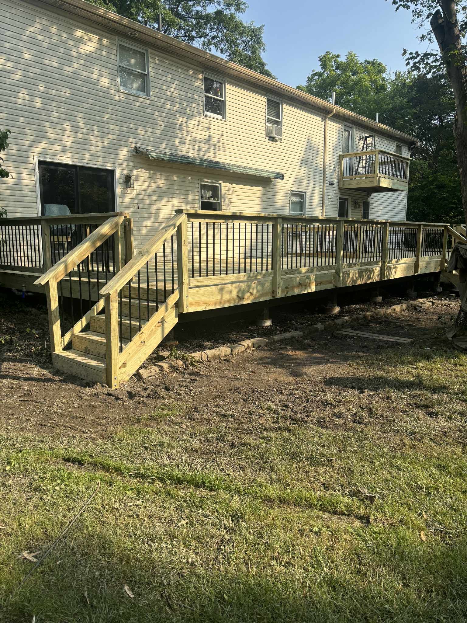 Wooden deck attached to a two-story house, with black railings.