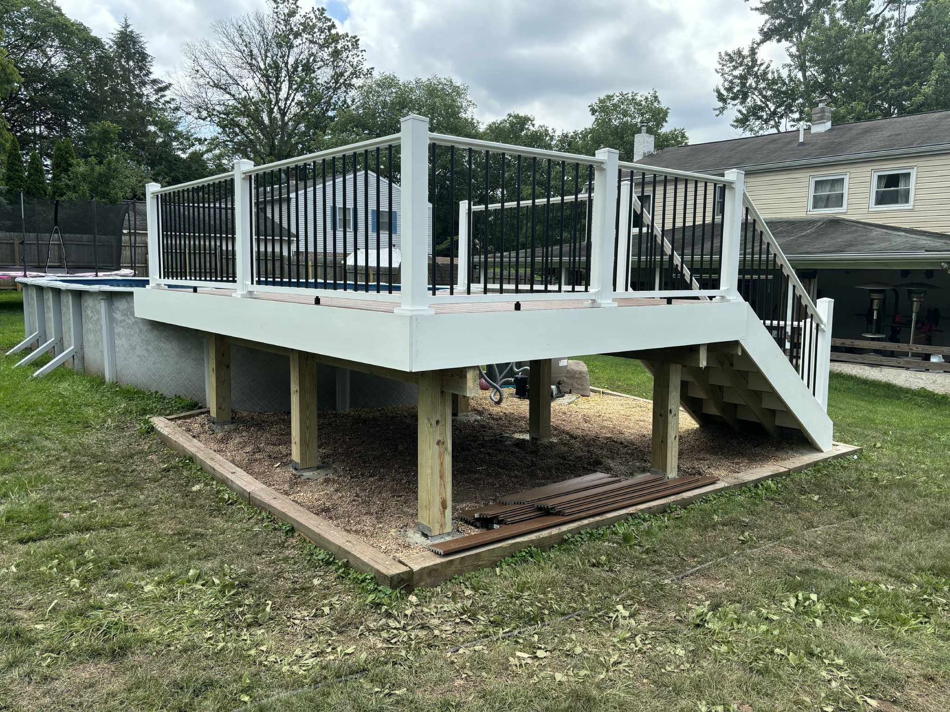 A raised deck with black railings and white posts, next to an above-ground pool, in a backyard.