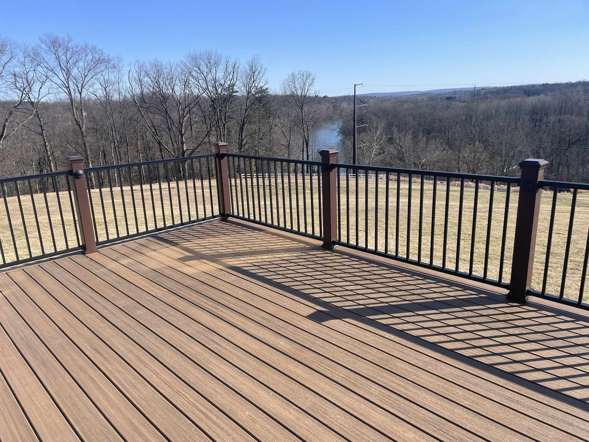 Wooden deck with black railings overlooking a river and treeline. Sunny day.