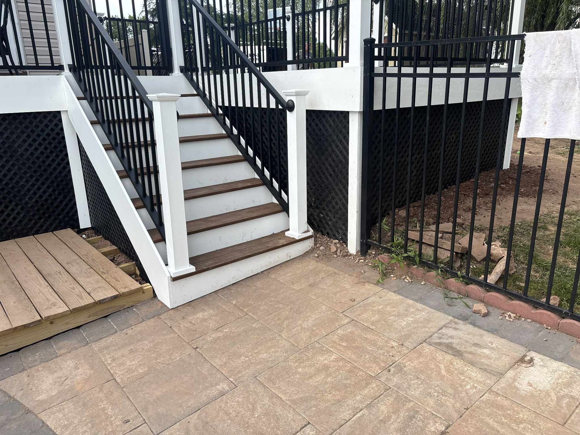 Stairs with white stringers, brown steps, and black railings leading up to a deck with black lattice.