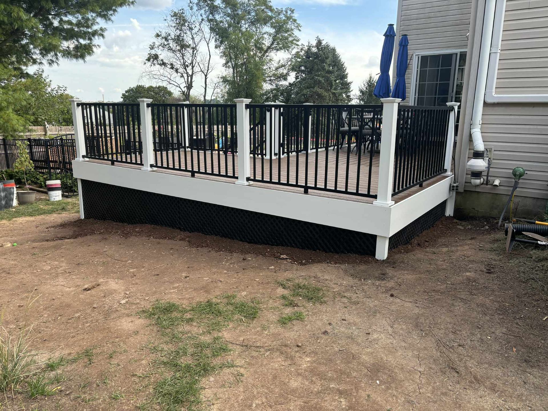 A newly built deck with black railings and a white frame sits outside a house on a gravel yard.