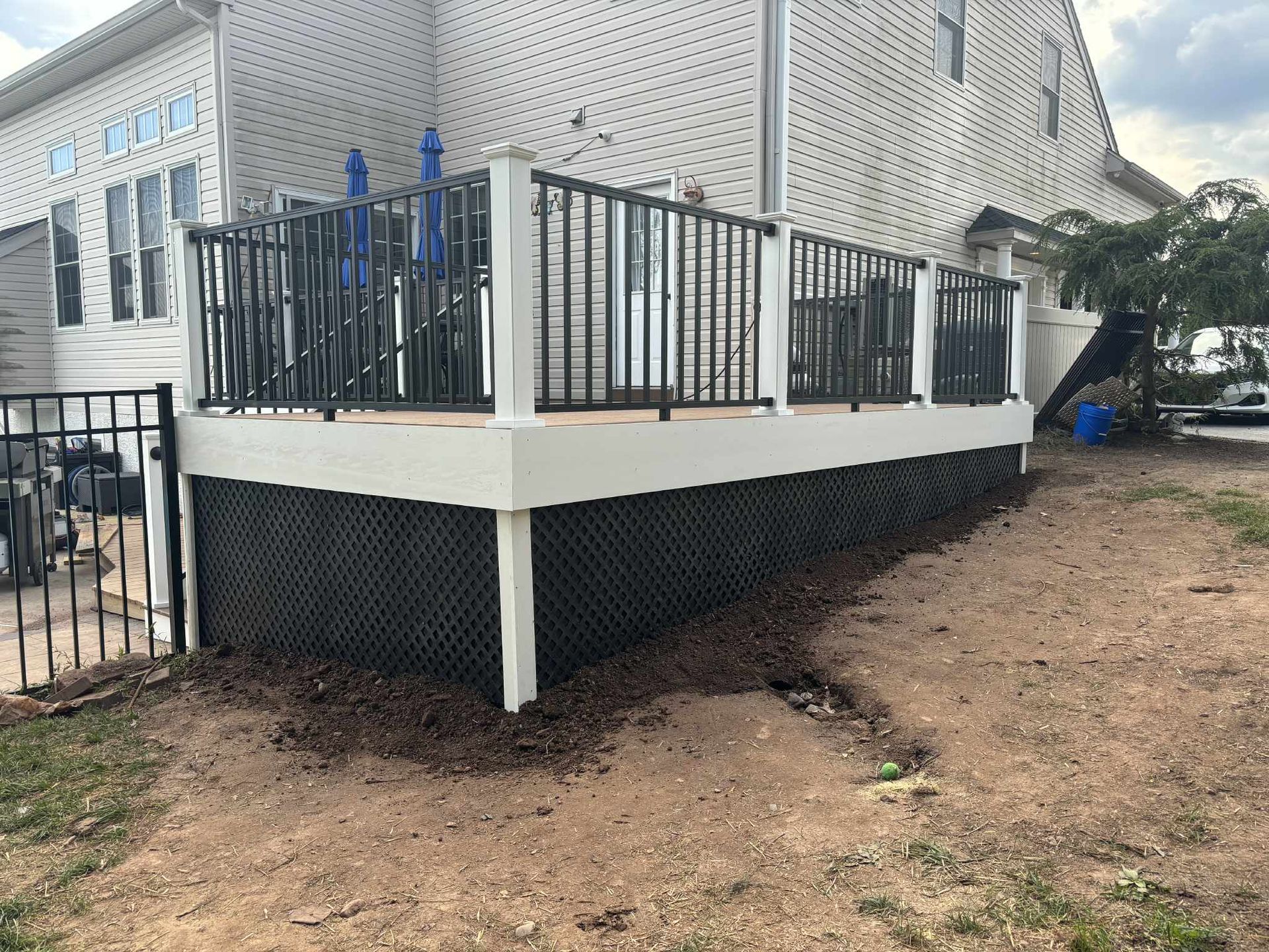 Deck with white trim, black railings, and lattice skirting, adjacent to a house.
