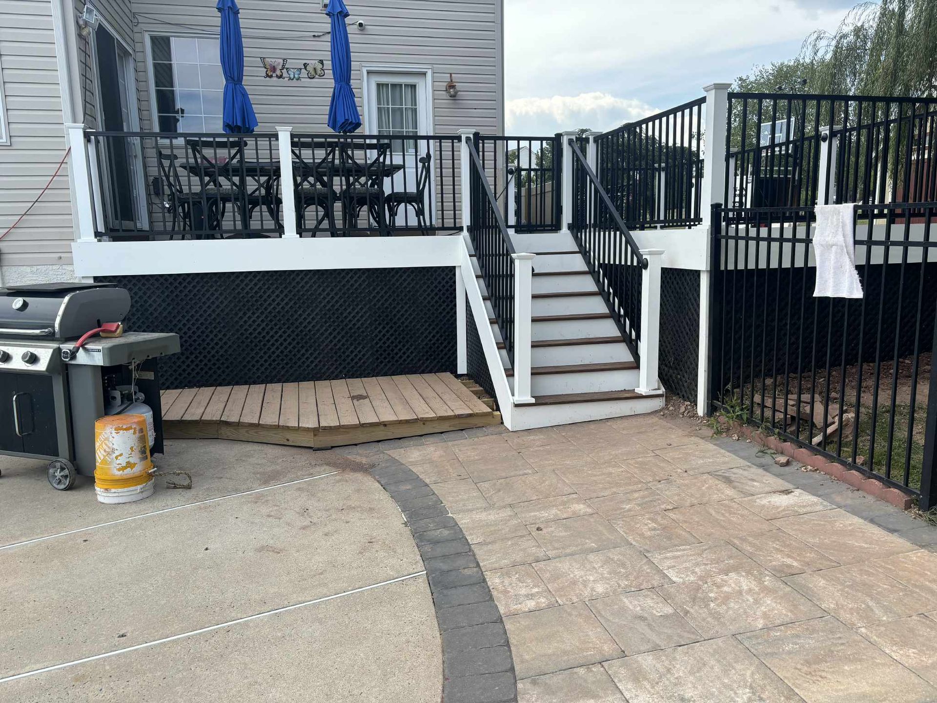 Backyard deck with stairs, black metal fence, barbecue grill, and concrete patio.