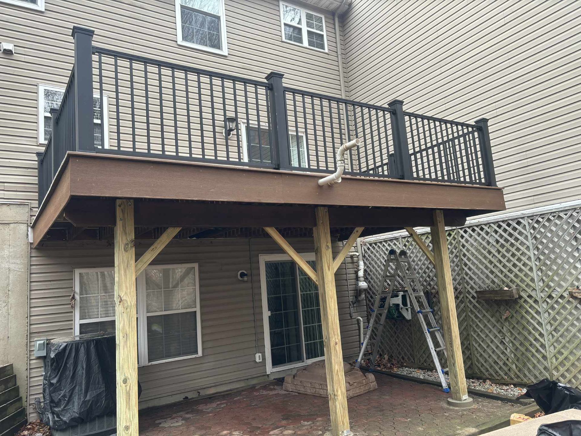 Two-story deck attached to a house; black railing, brown decking, supported by wooden posts.