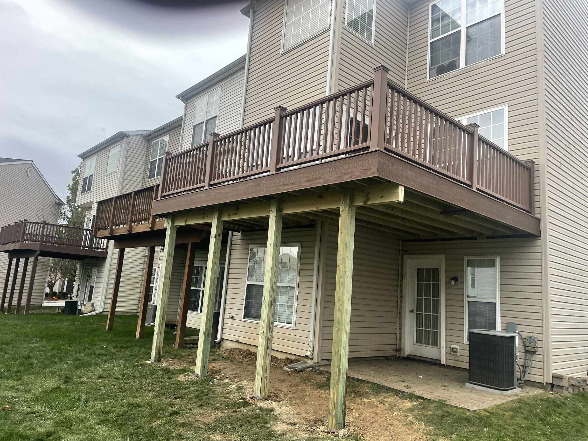 Multi-level brown wooden decks on a multi-story beige building, supported by wood posts, over a grassy lawn.