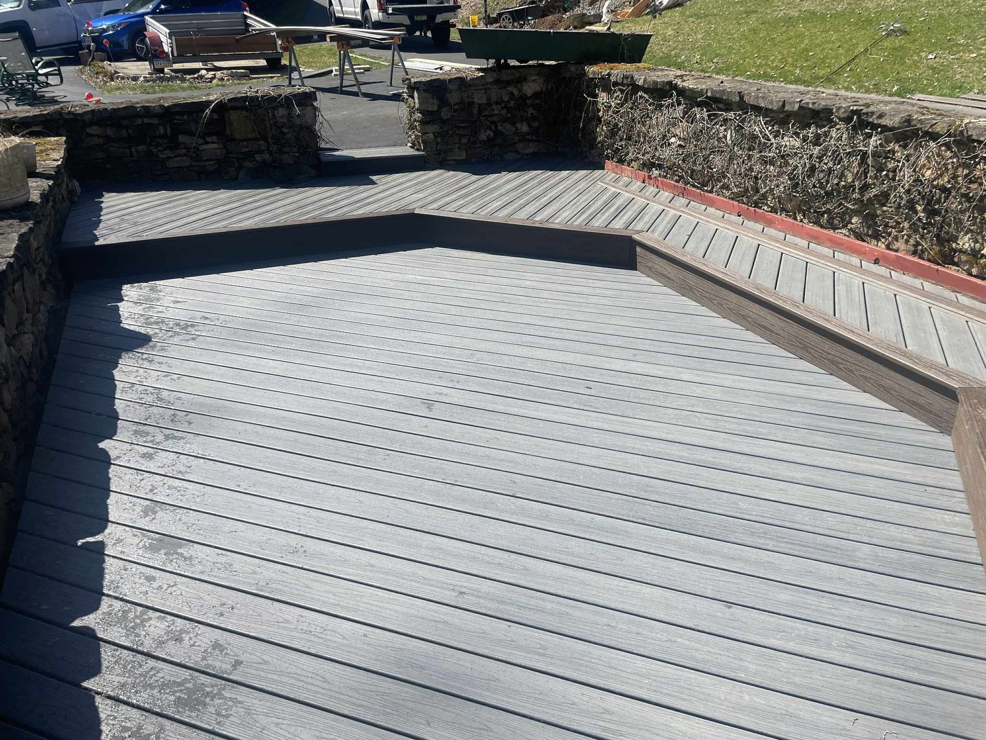 Gray patio with a stone wall and access to a pathway, viewed from above.