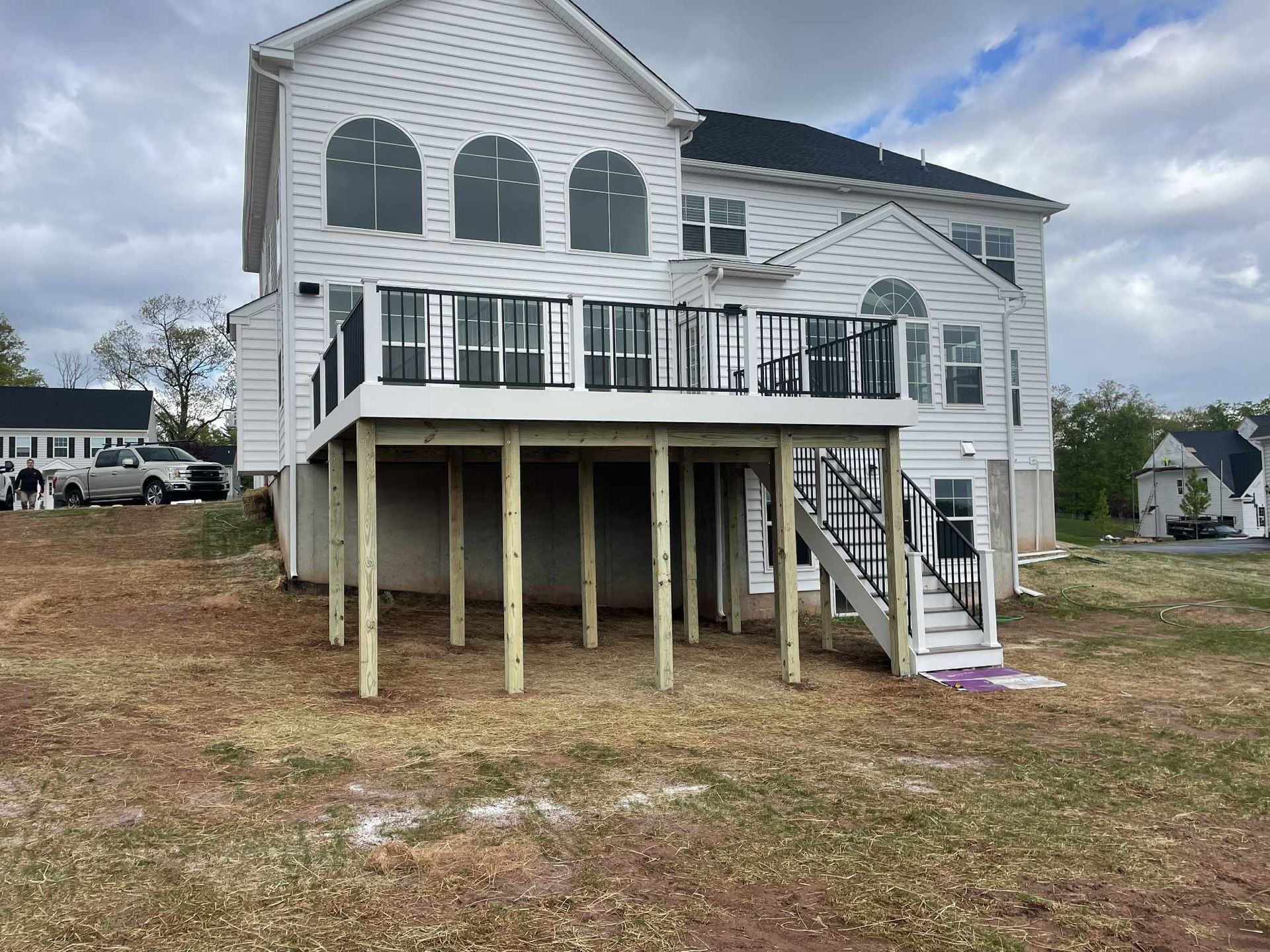 Rear view of a white house with a two-level deck on wooden posts; black railings and stairs.