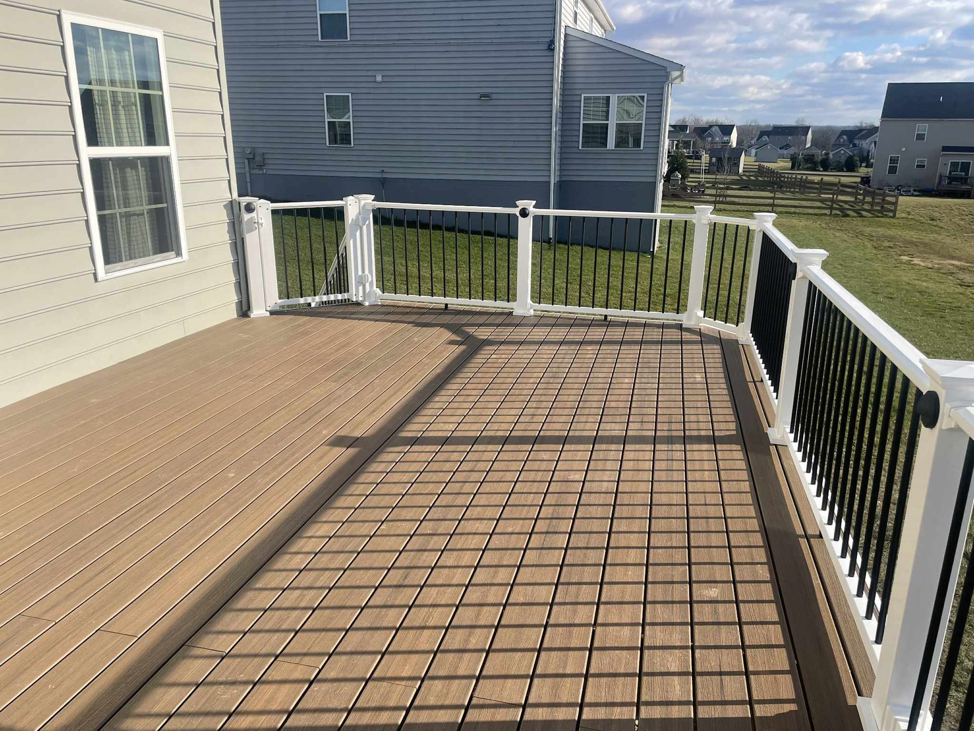Wooden deck with black railing and white posts on a sunny day.