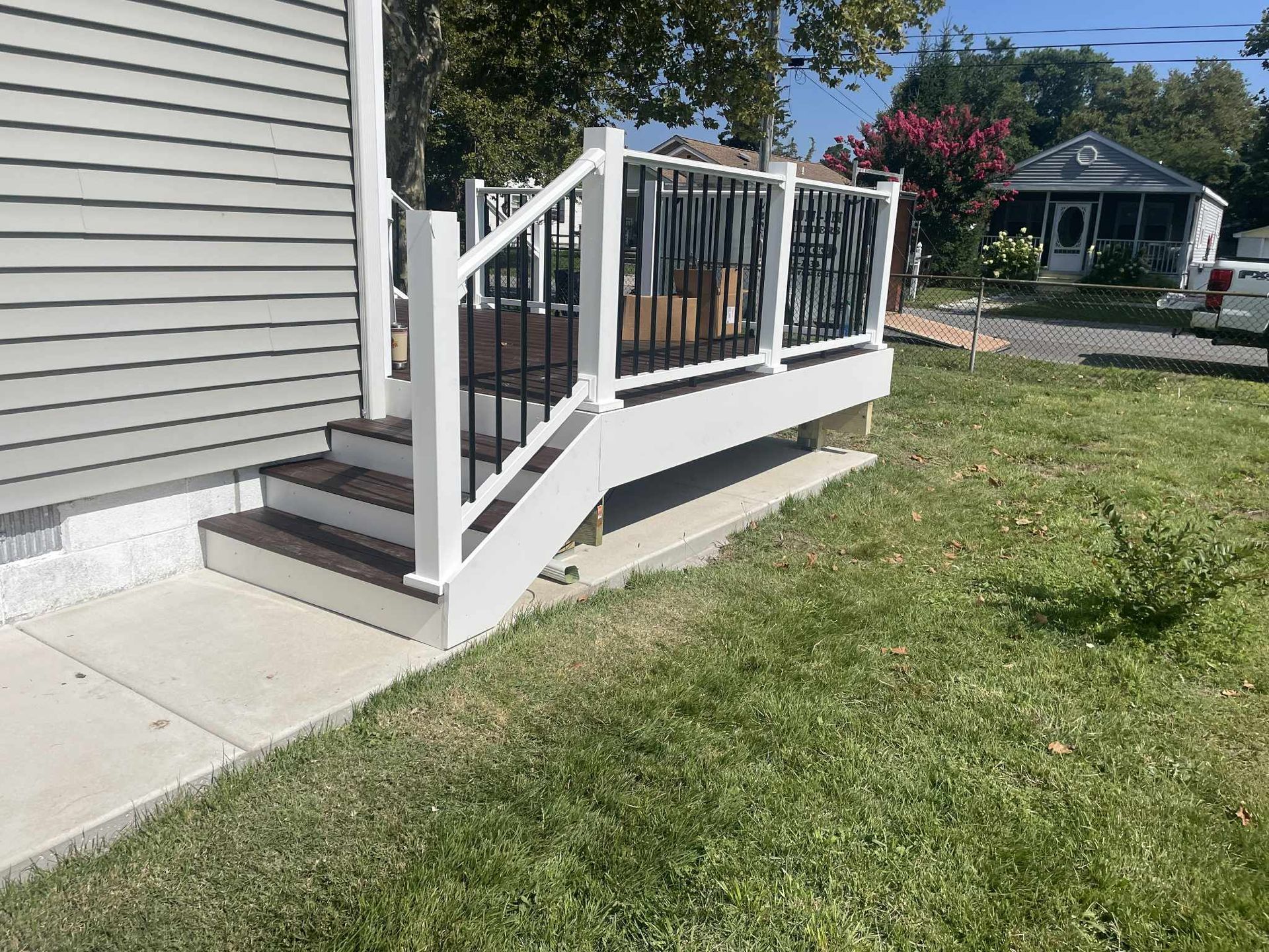 Gray siding and a white deck with black railings and steps. Concrete path and grassy yard.