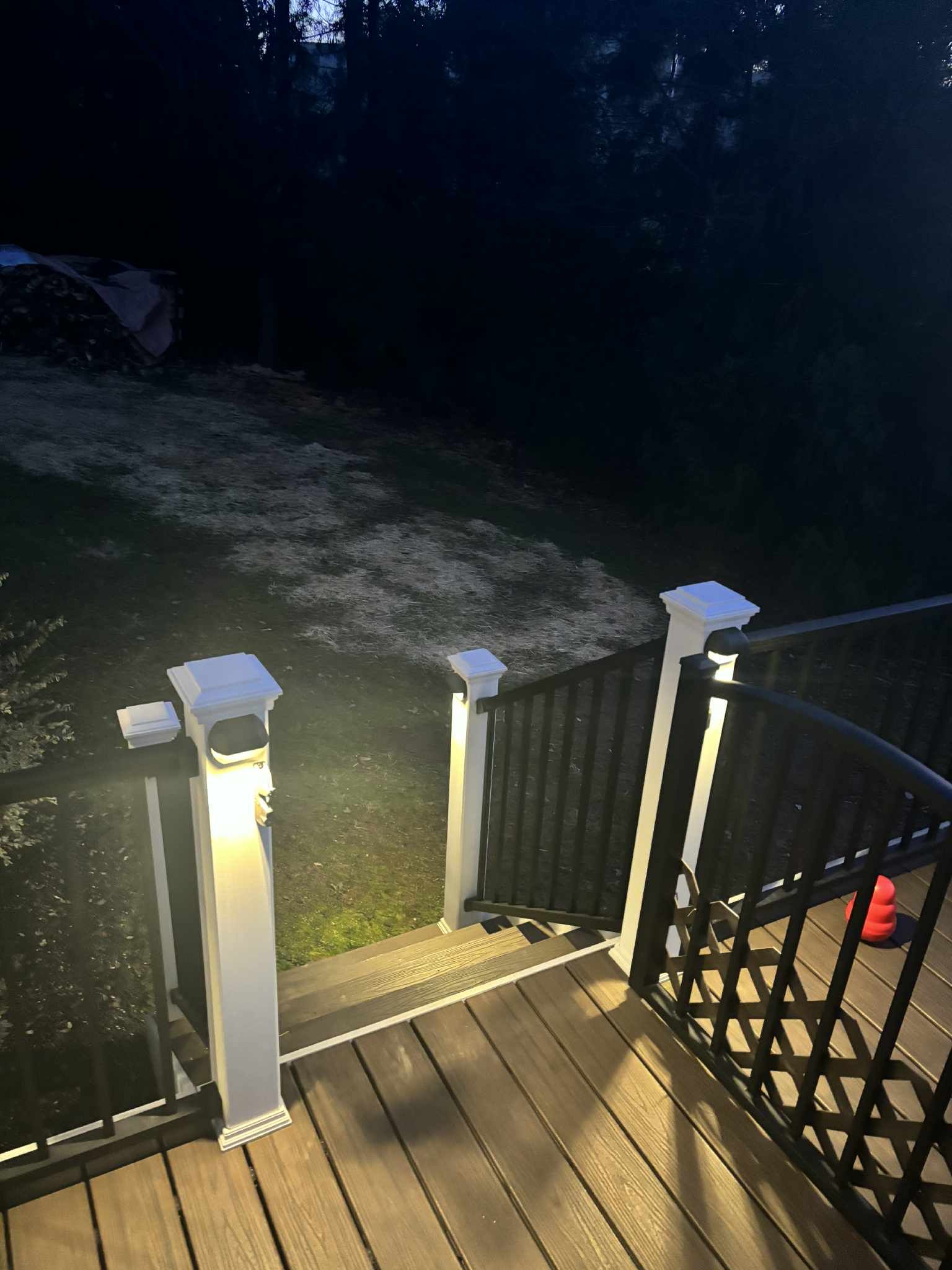 Deck at night with lit posts and railing, overlooking a dark yard.