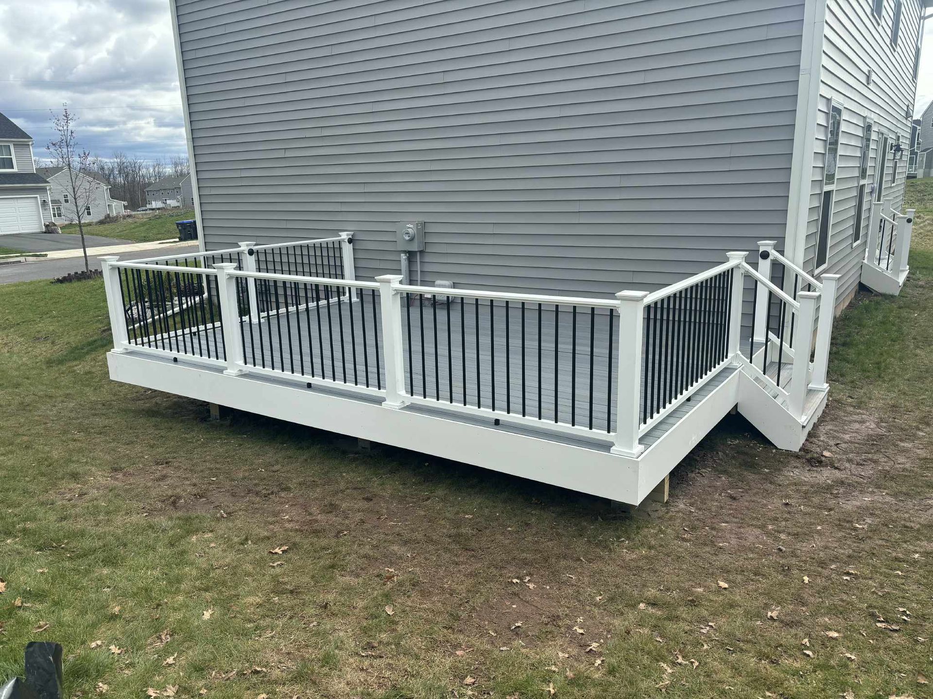 Gray house with white deck, black railing, on a grassy yard.