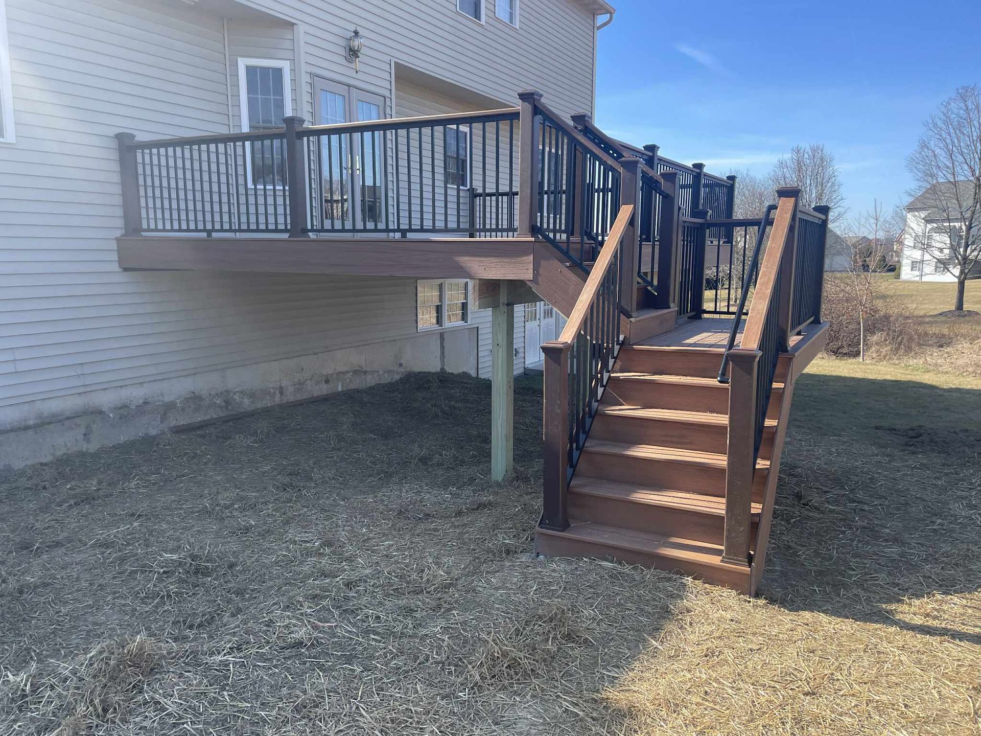Wooden deck with stairs attached to a two-story house, overlooking a grassy area.