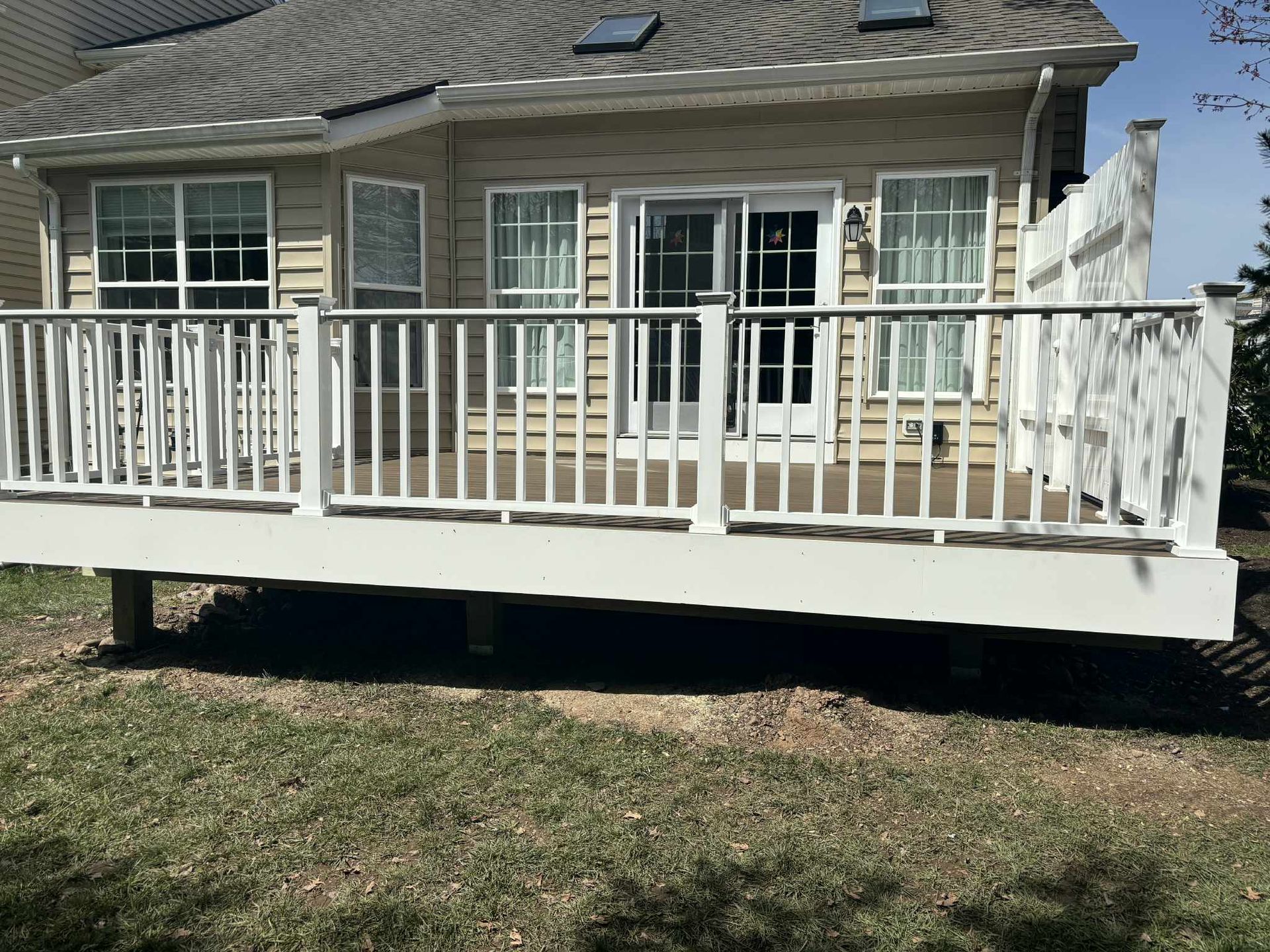 White deck attached to a light-colored house with sliding glass doors and windows, overlooking a grassy yard.