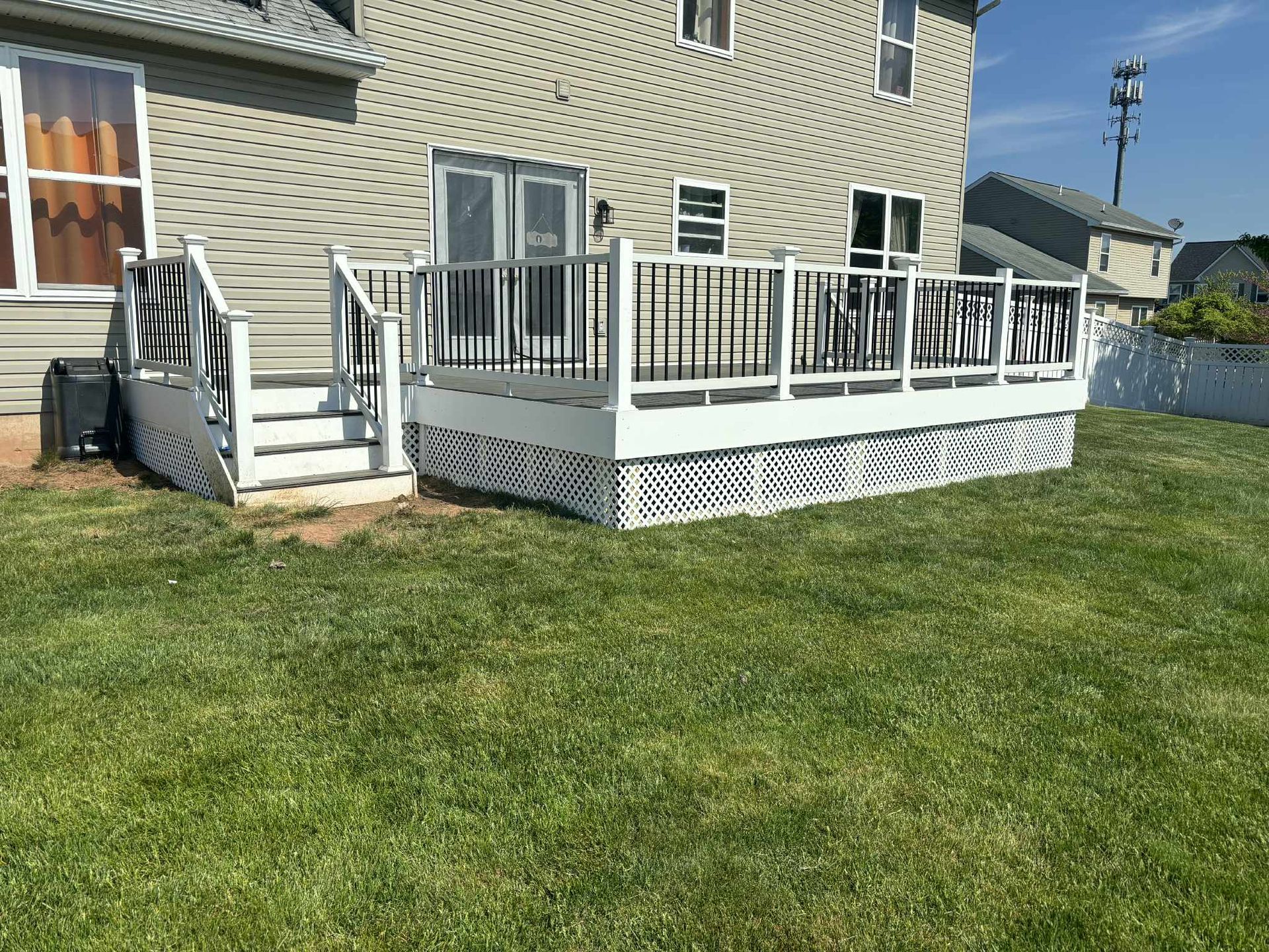 Backyard deck with white lattice and railings, connected to a house with a door and windows, surrounded by green grass.
