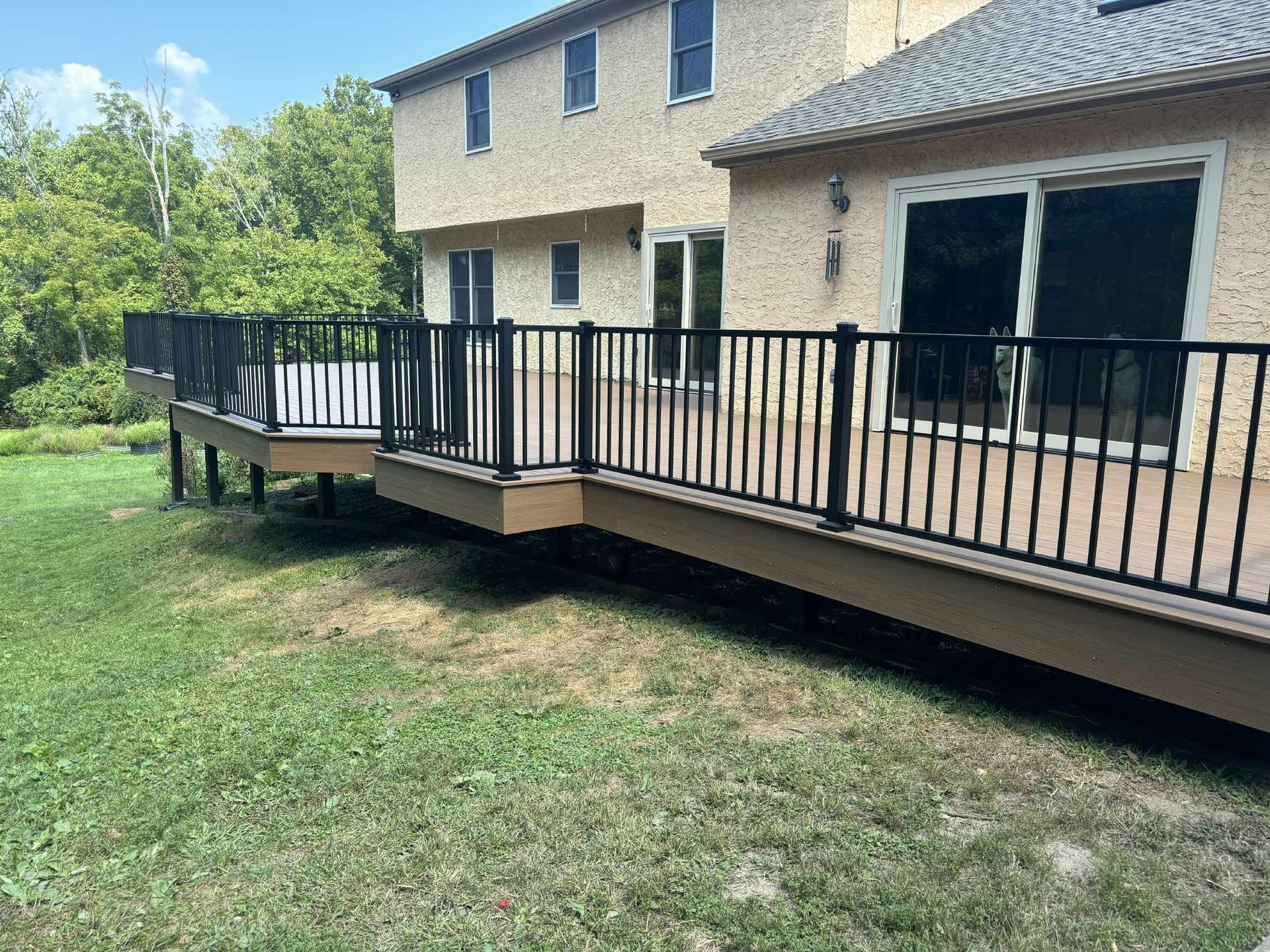 Backyard deck with black railing and composite decking, attached to a light-colored house.