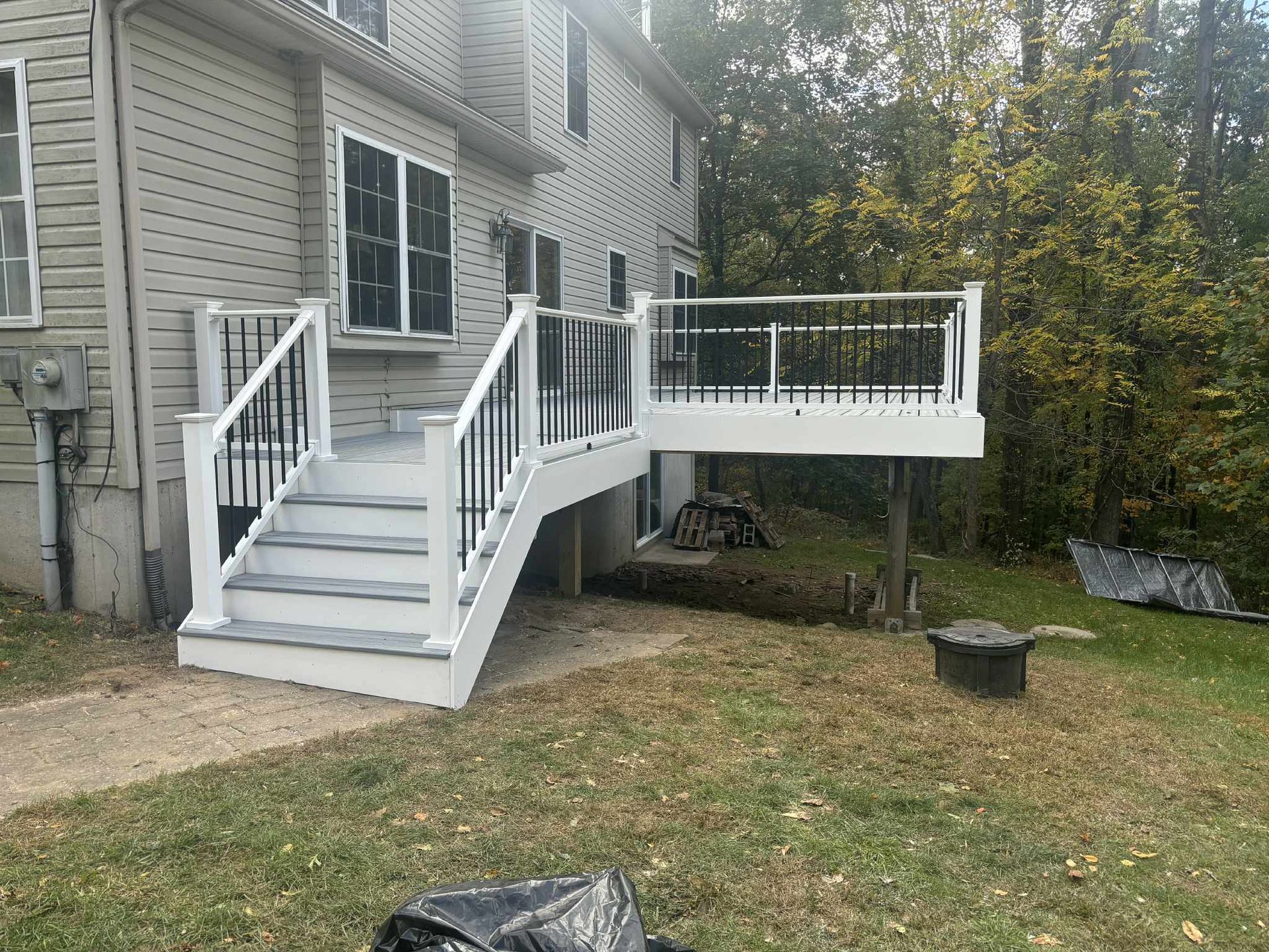 Gray and white deck with black railings on a two-story house, set in a grassy yard.