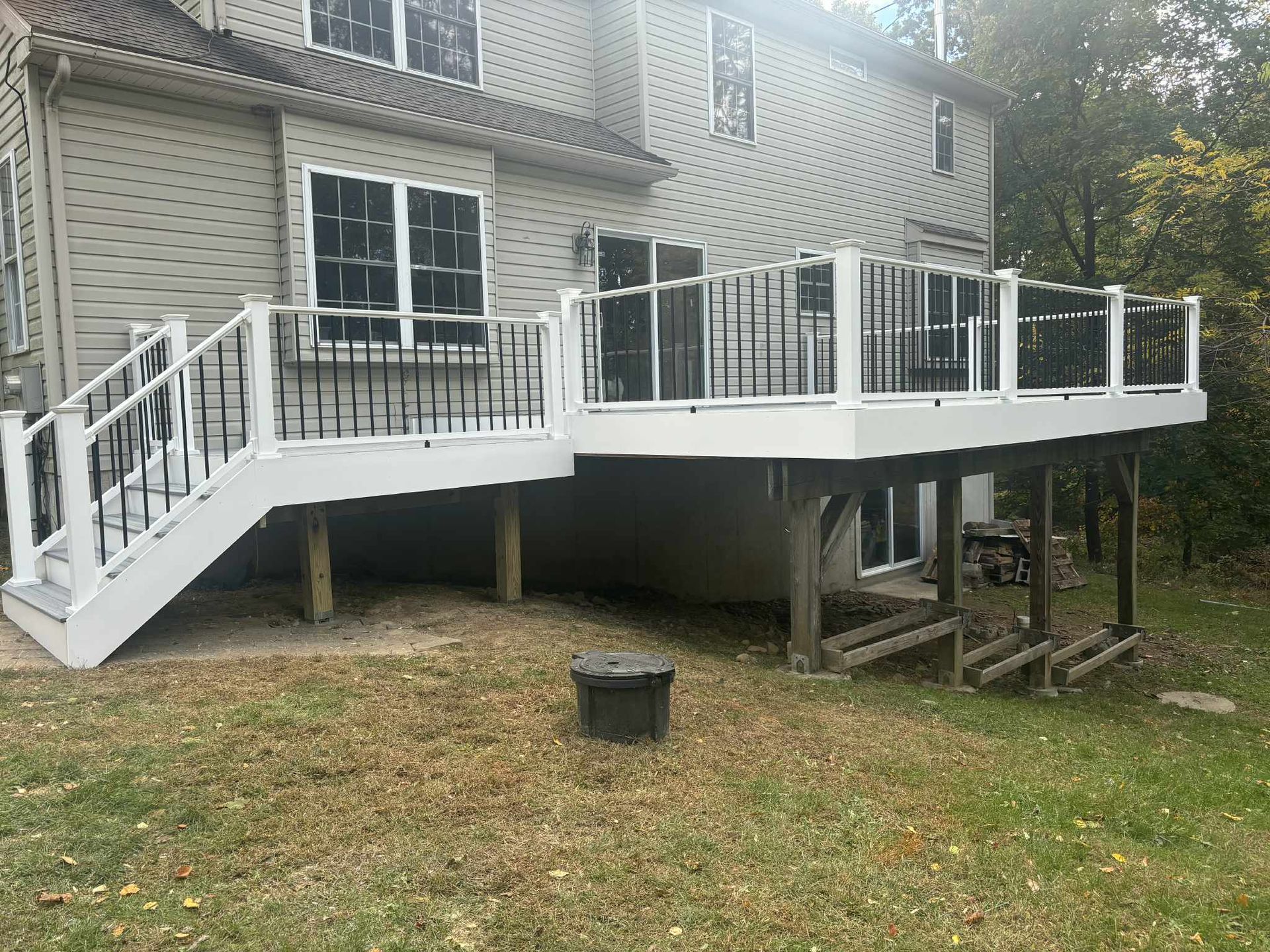 Two-level deck attached to a house with black railings and white trim. Overlooking a grassy yard.