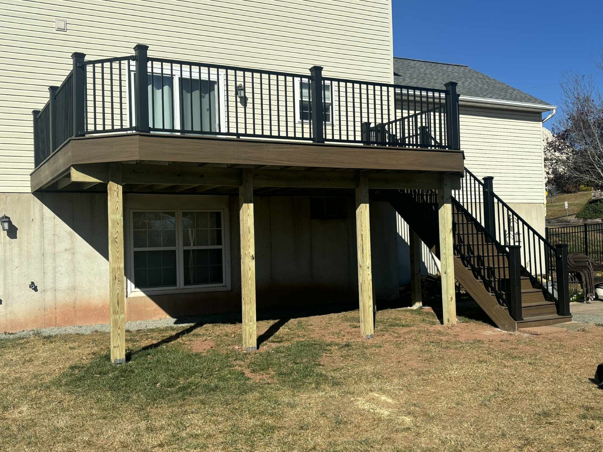 Elevated wooden deck attached to a house with black railings and stairs; brown composite decking.