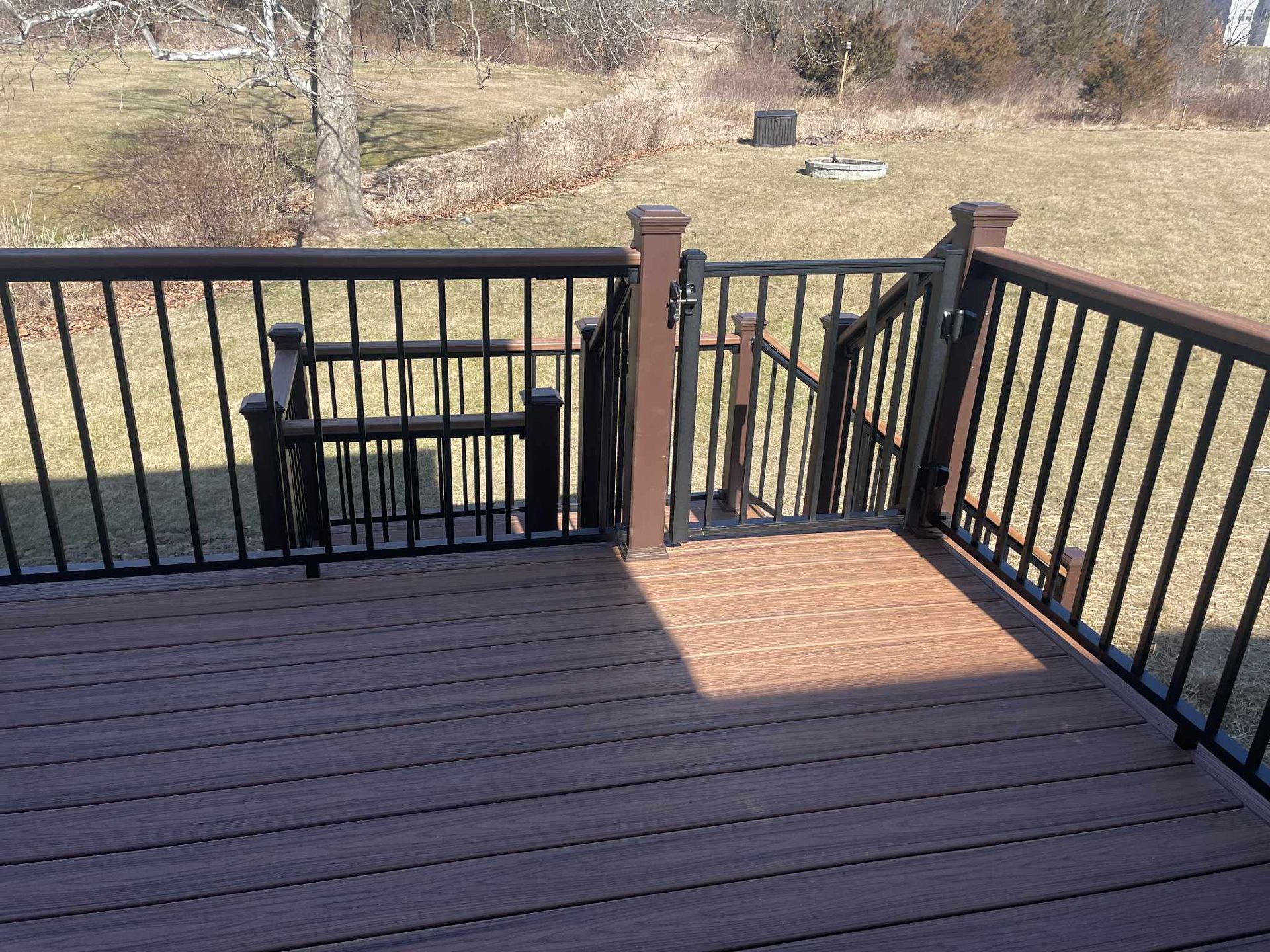 Brown deck with black railing and gate, leading to a grassy yard.