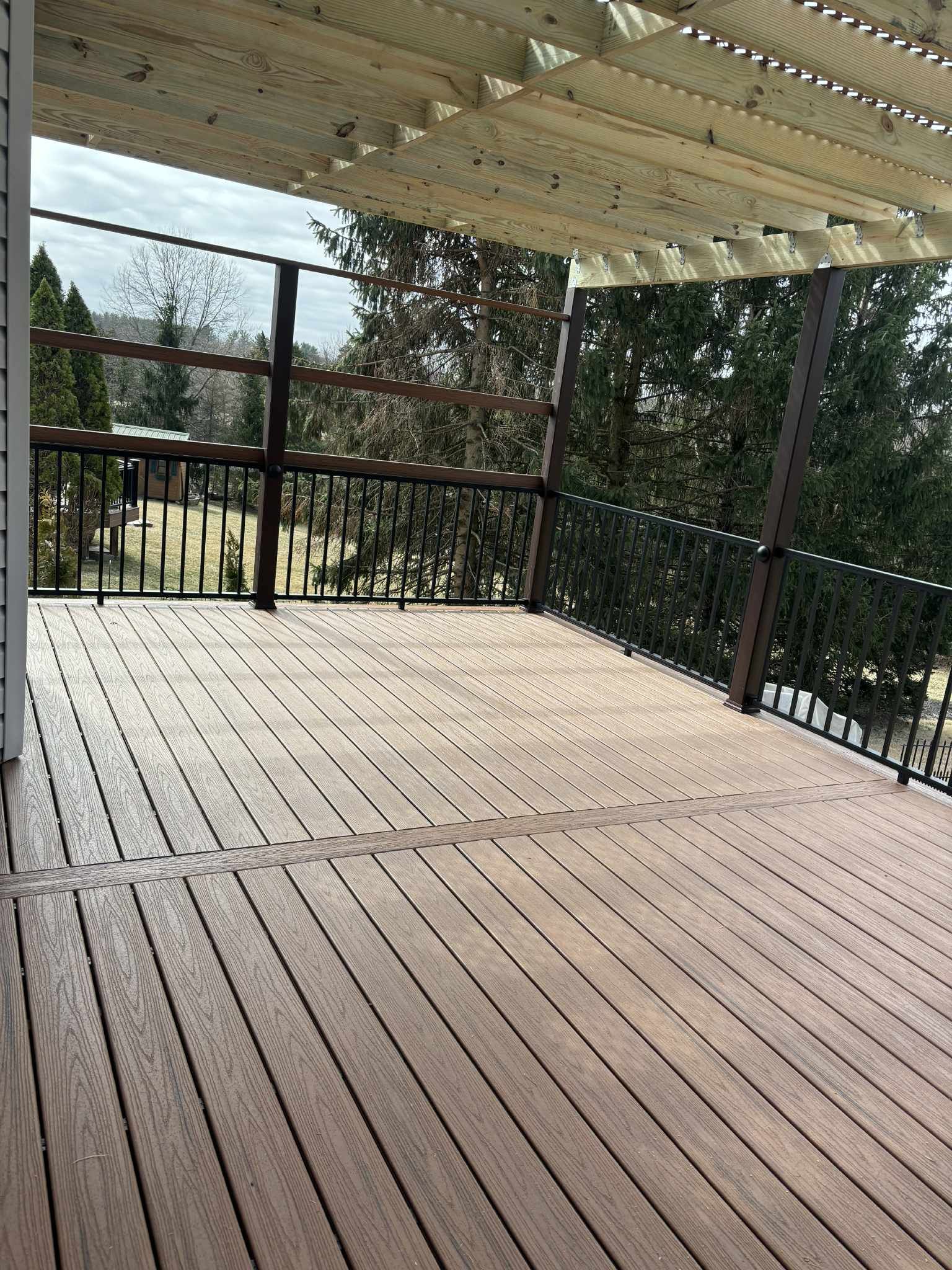 Wooden deck with railing, overhead sun shade, overlooking a wooded area.