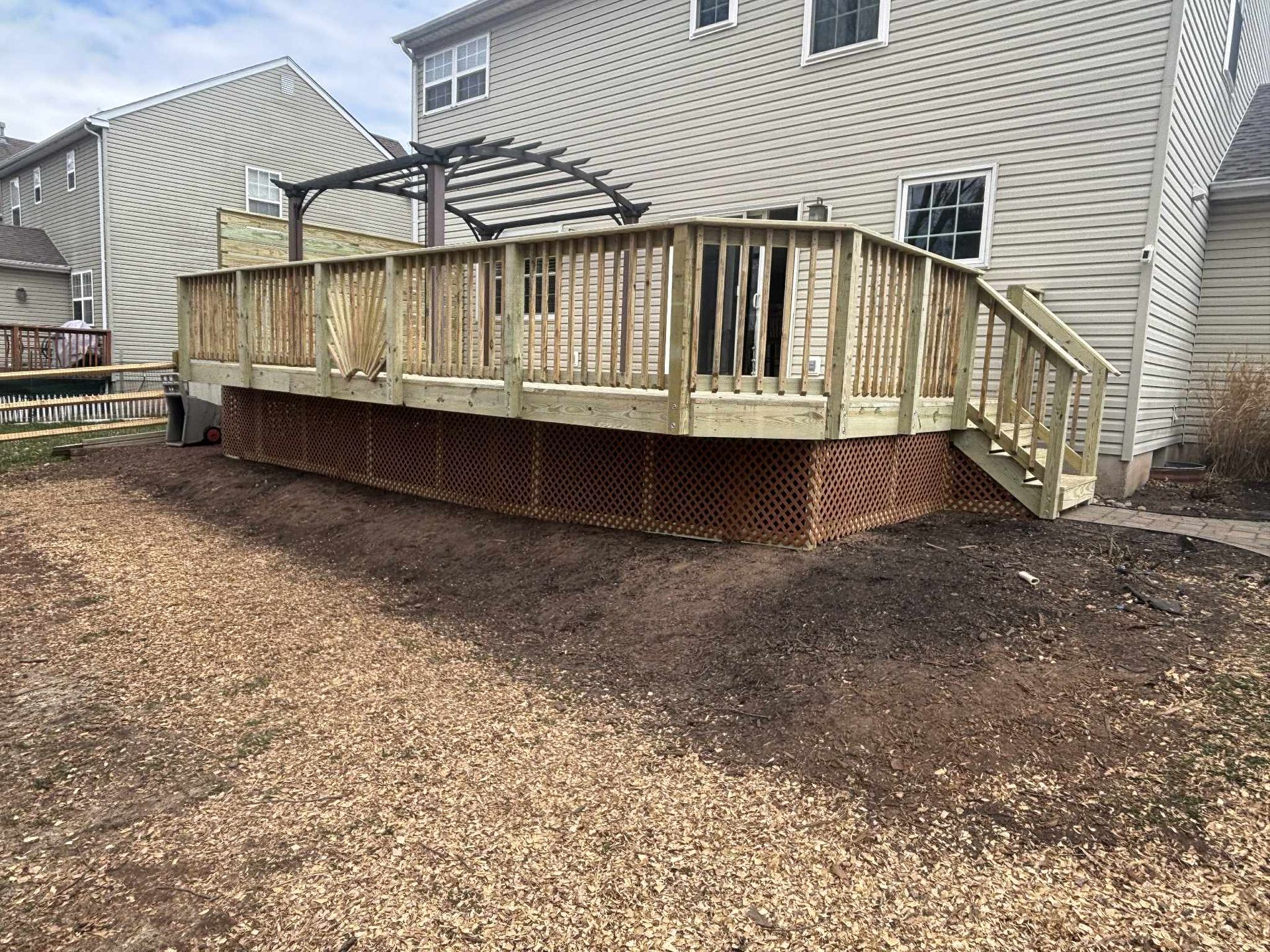 Wooden deck with lattice skirting, attached to a light-colored house. Brown mulch ground.