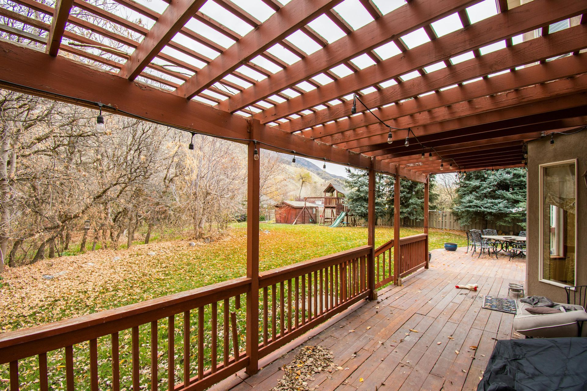 Wooden deck with pergola, overlooking yard with fall foliage and trees.