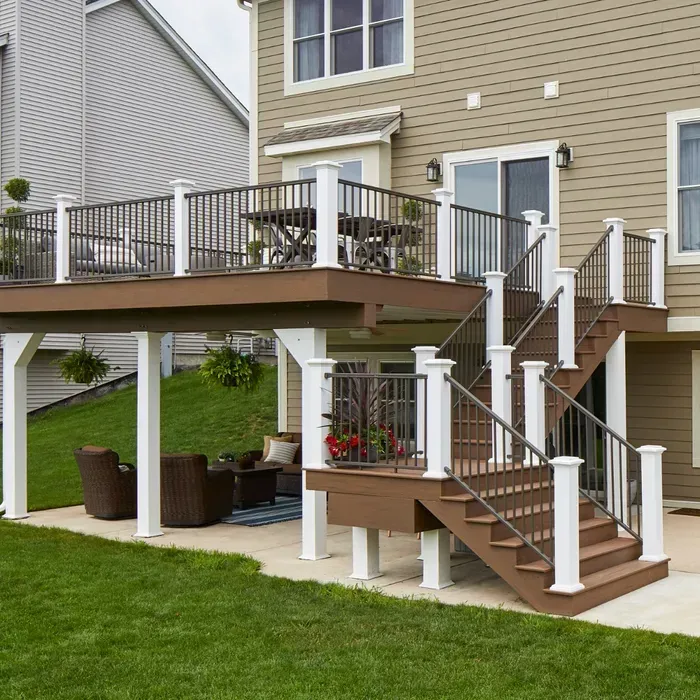 Two-story deck with brown decking, white posts, and metal railings on a house with a green lawn.