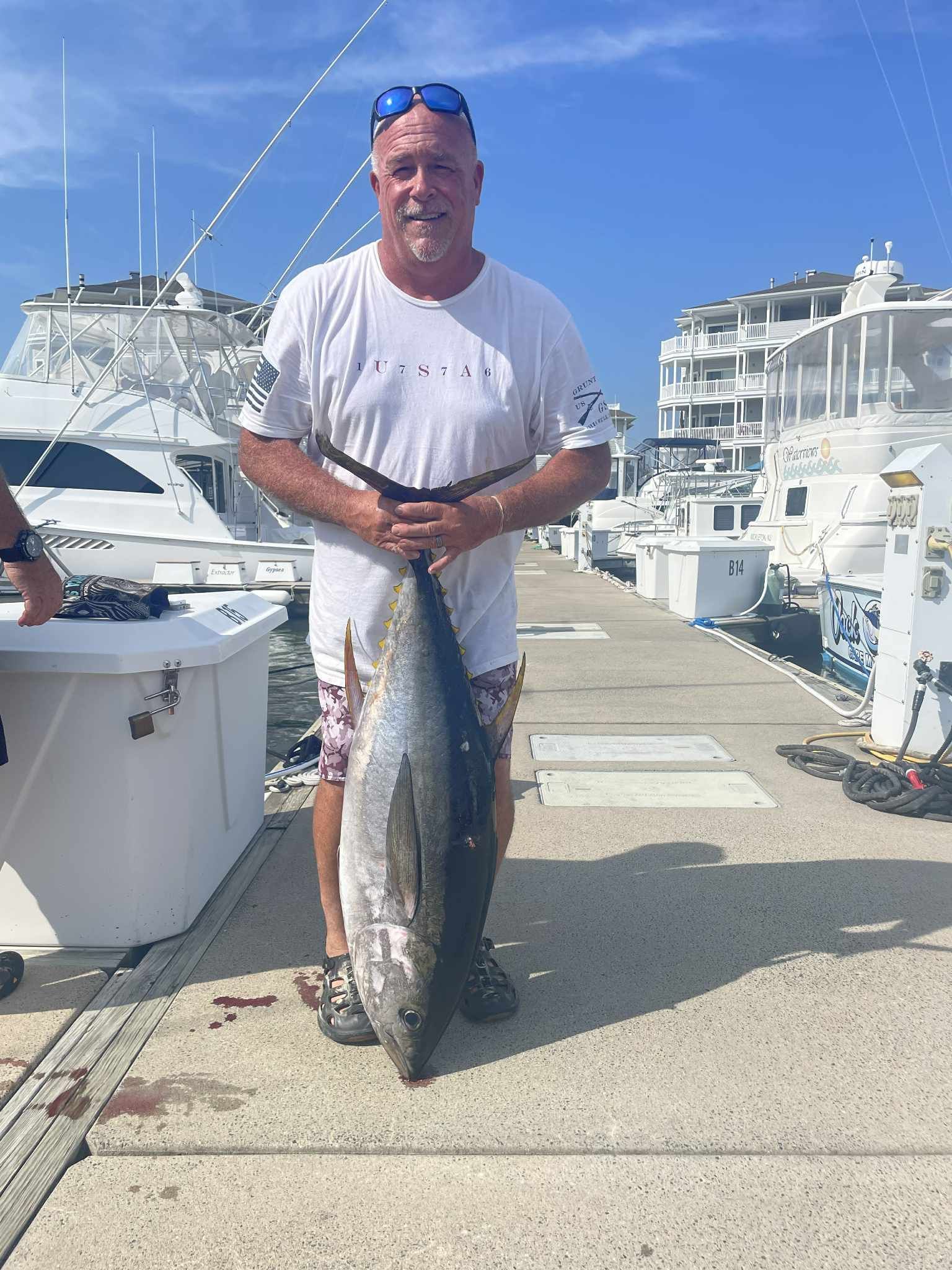 Man holding large fish on a dock, boats in background.