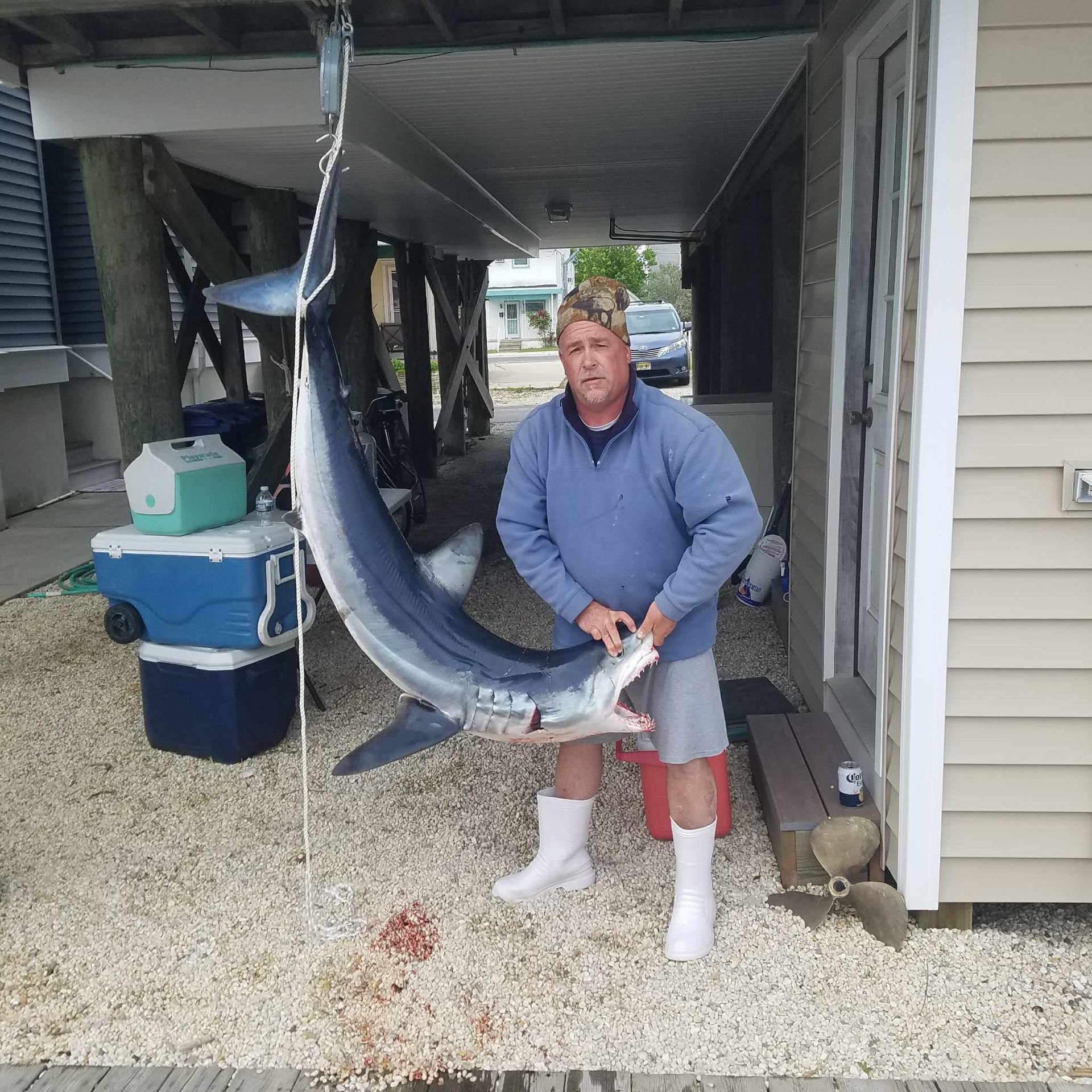 Man holding a large, dead swordfish hanging from a hook beneath a building.