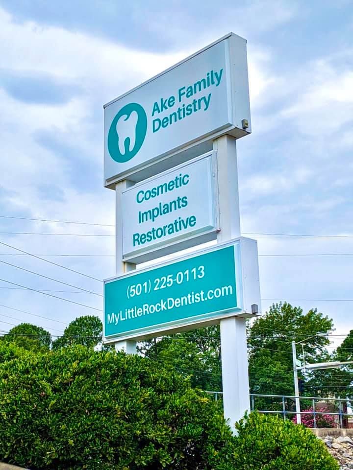 a large sign for a dentist 's office is surrounded by trees .