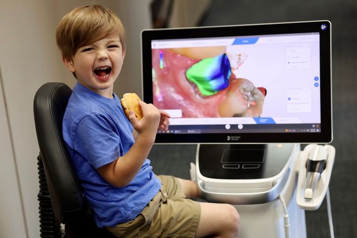 a young boy is sitting in front of a computer screen eating a cookie .