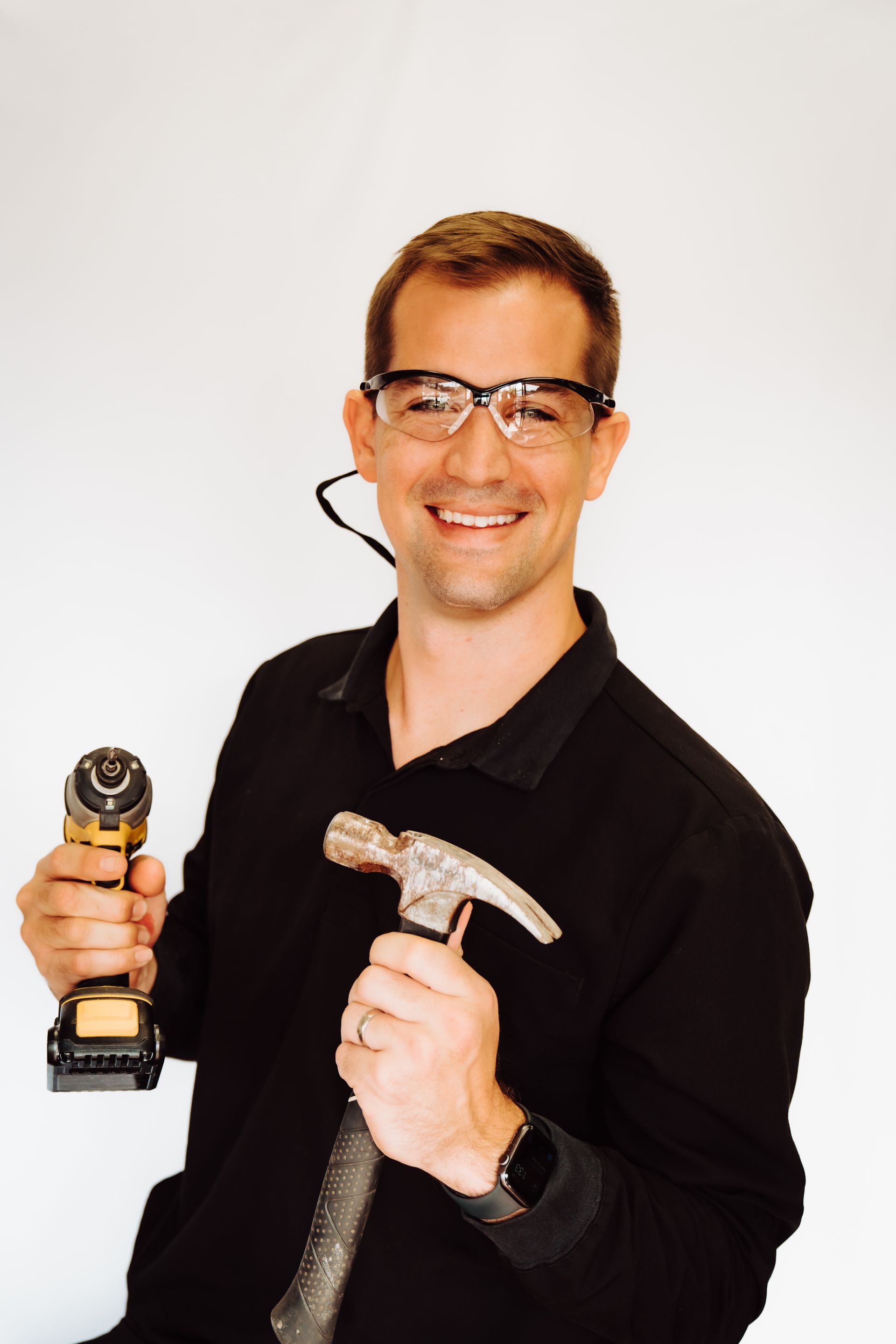 a man wearing glasses is holding a hammer and a drill .