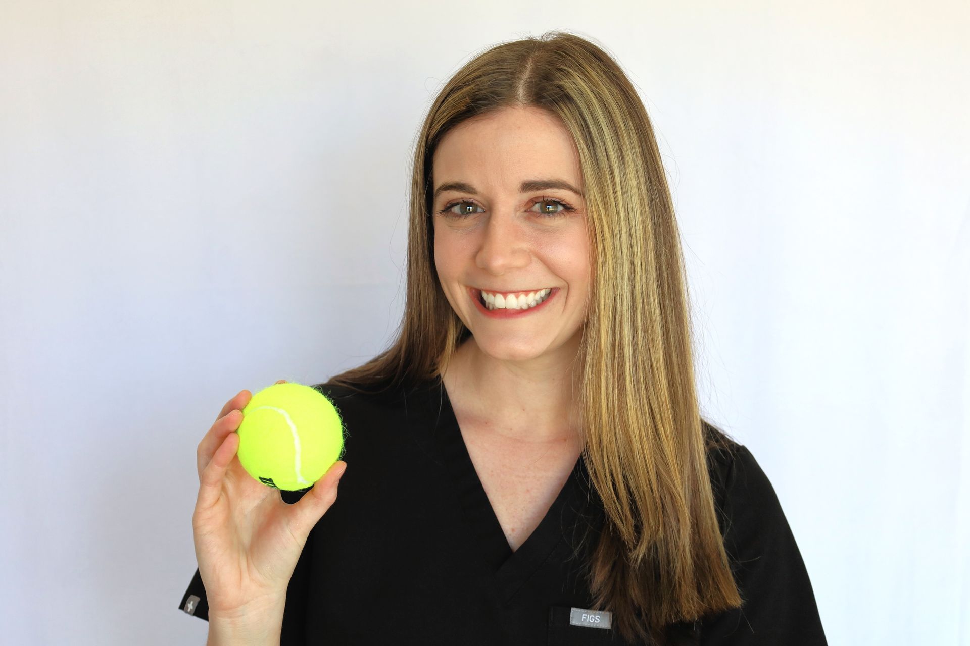 a woman in a black scrub top is holding a yellow tennis ball .