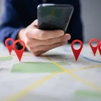 Hands holding a smartphone over a map marked with several red location pins.
