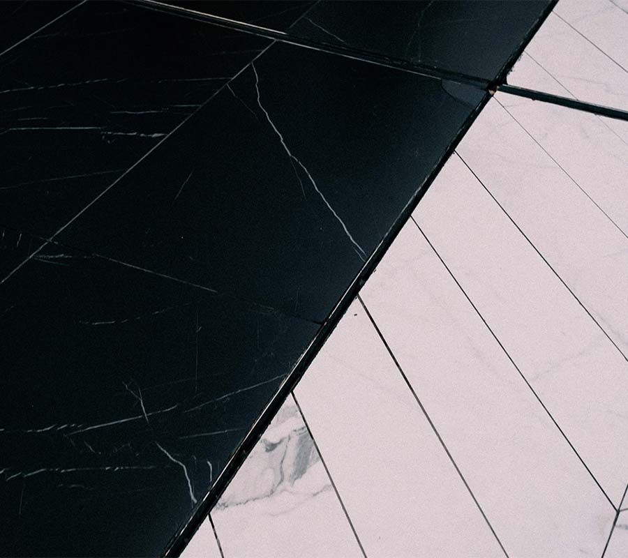A high-angle view showing a diagonal transition between black marble floor tiles and light, marble-veined tile planks.