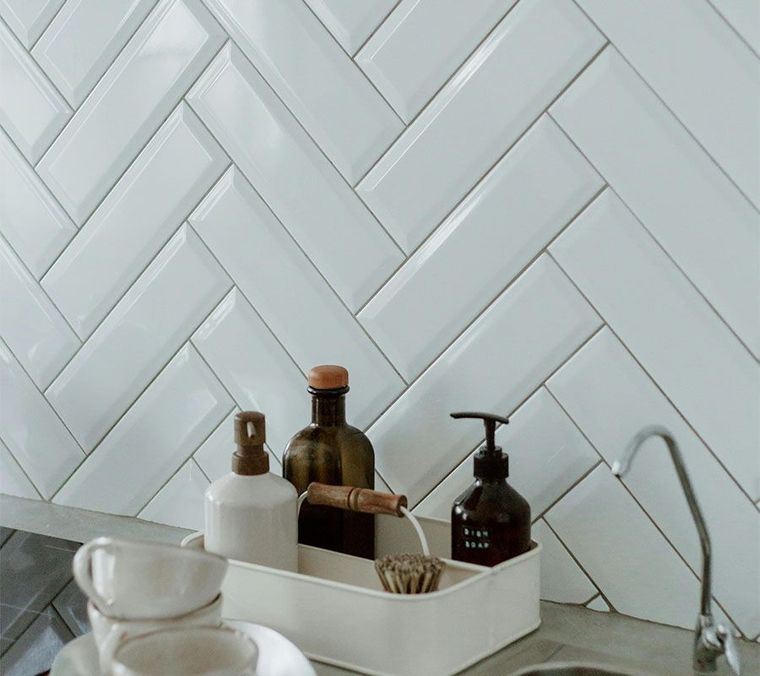 A kitchen sink area with white subway tiles in a herringbone pattern, a storage tray with bottles, and a faucet.