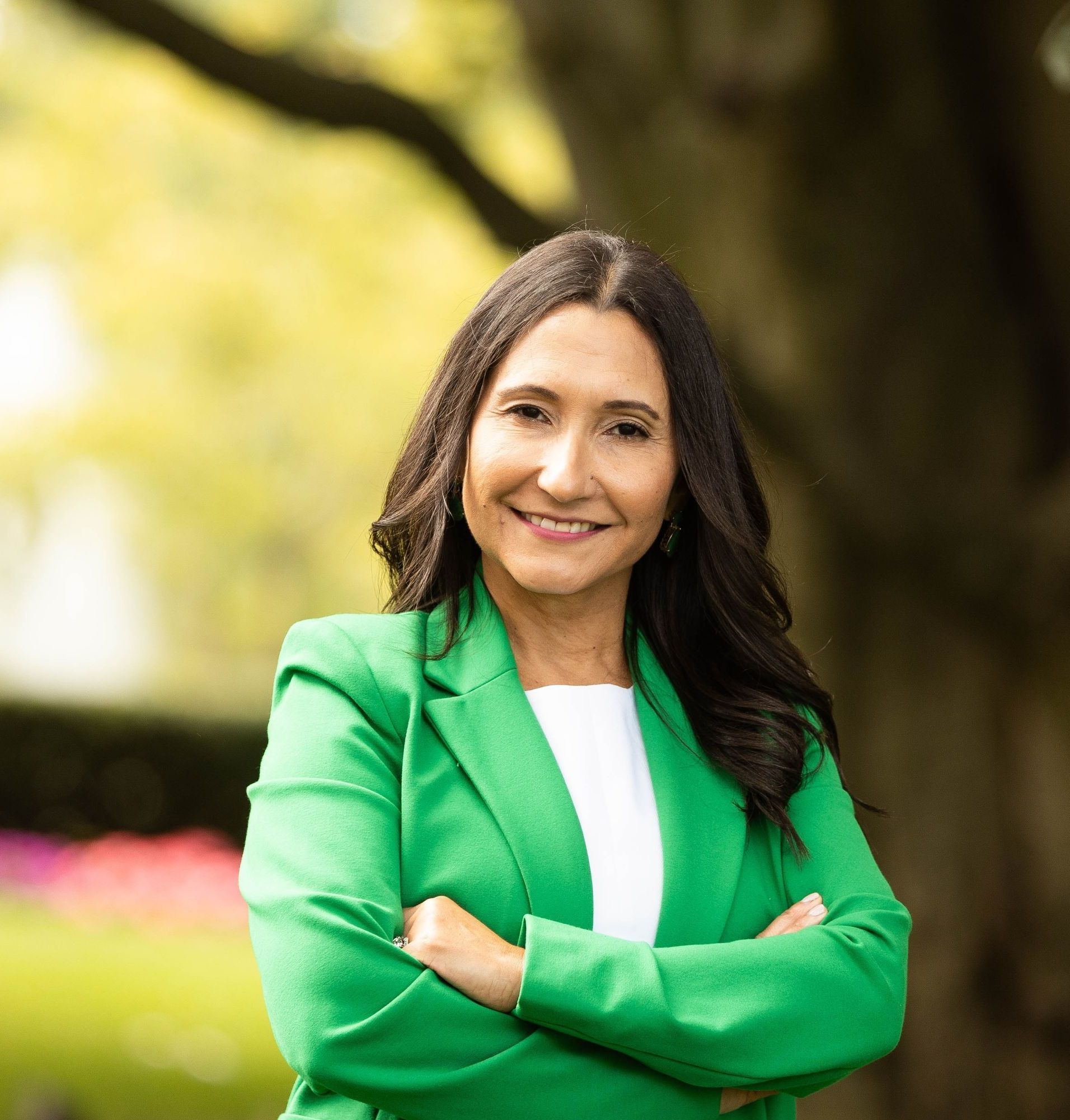 Woman with crossed arms in a green blazer smiles outside.