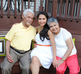 Woman with her grandparents on a wooden bench; the man wears yellow, the woman wears white, and the grandmother wears pink.