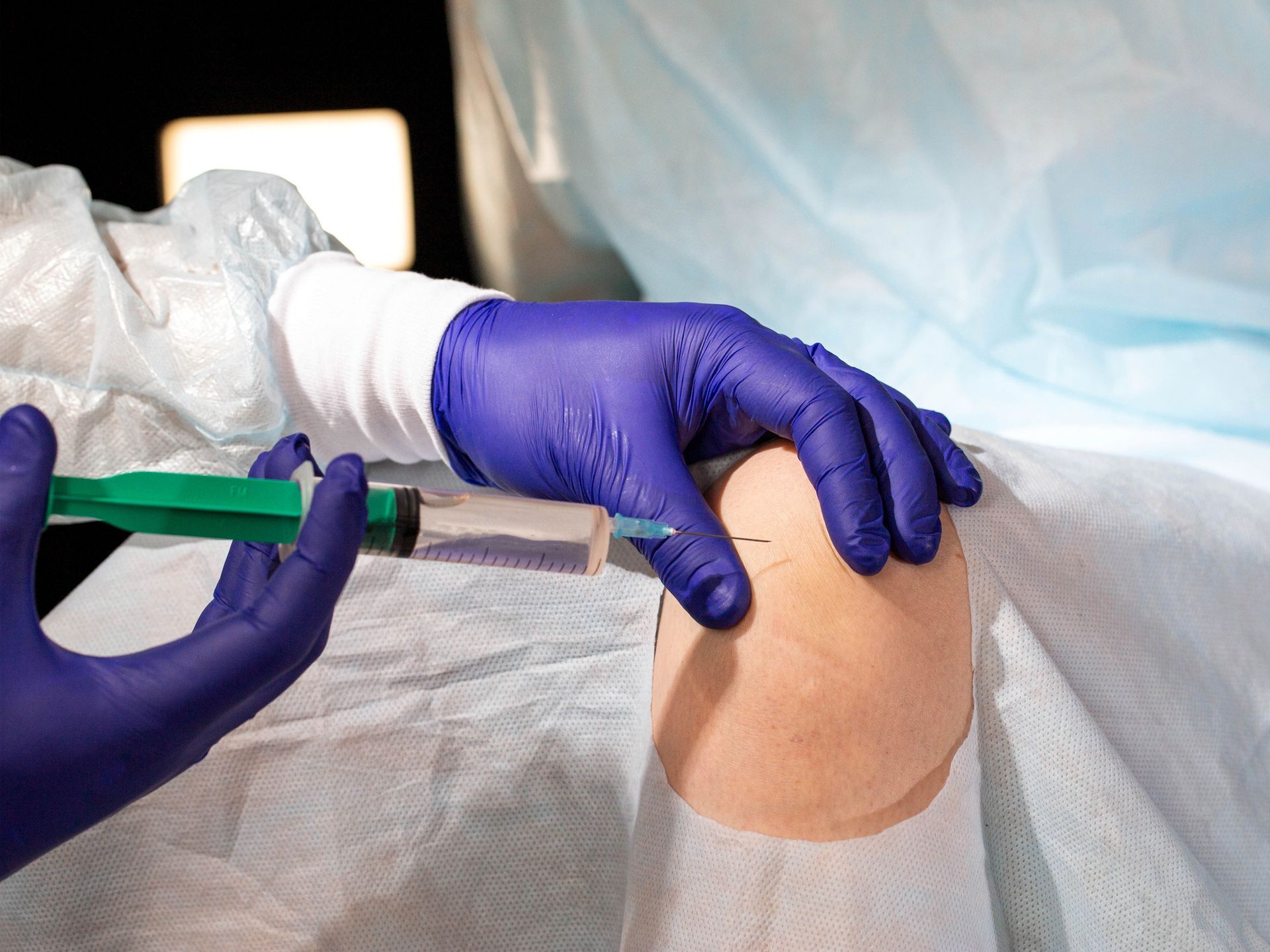 A person wearing purple gloves is holding a syringe in their hand.