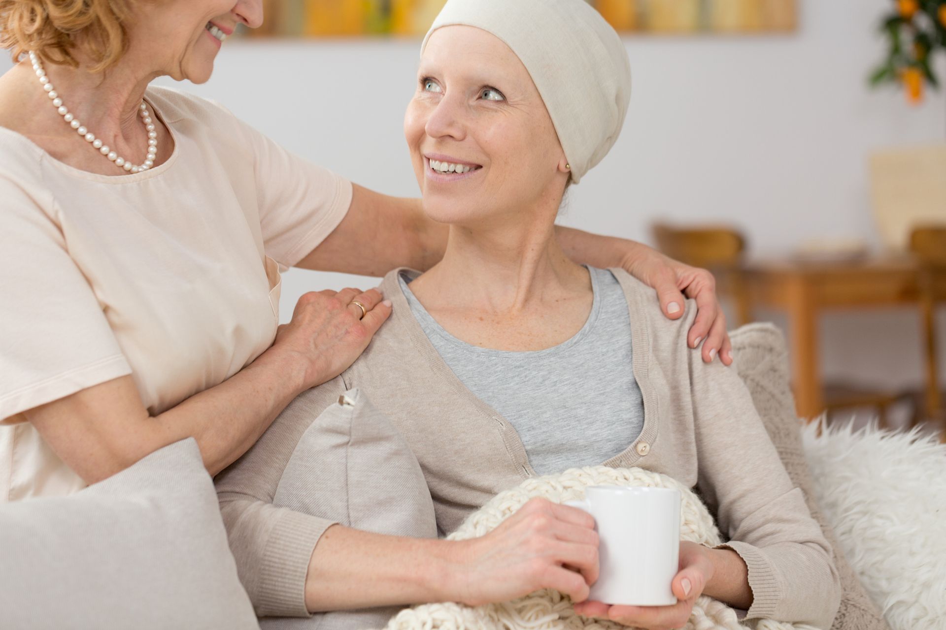 A woman with cancer is sitting on a couch with another woman.