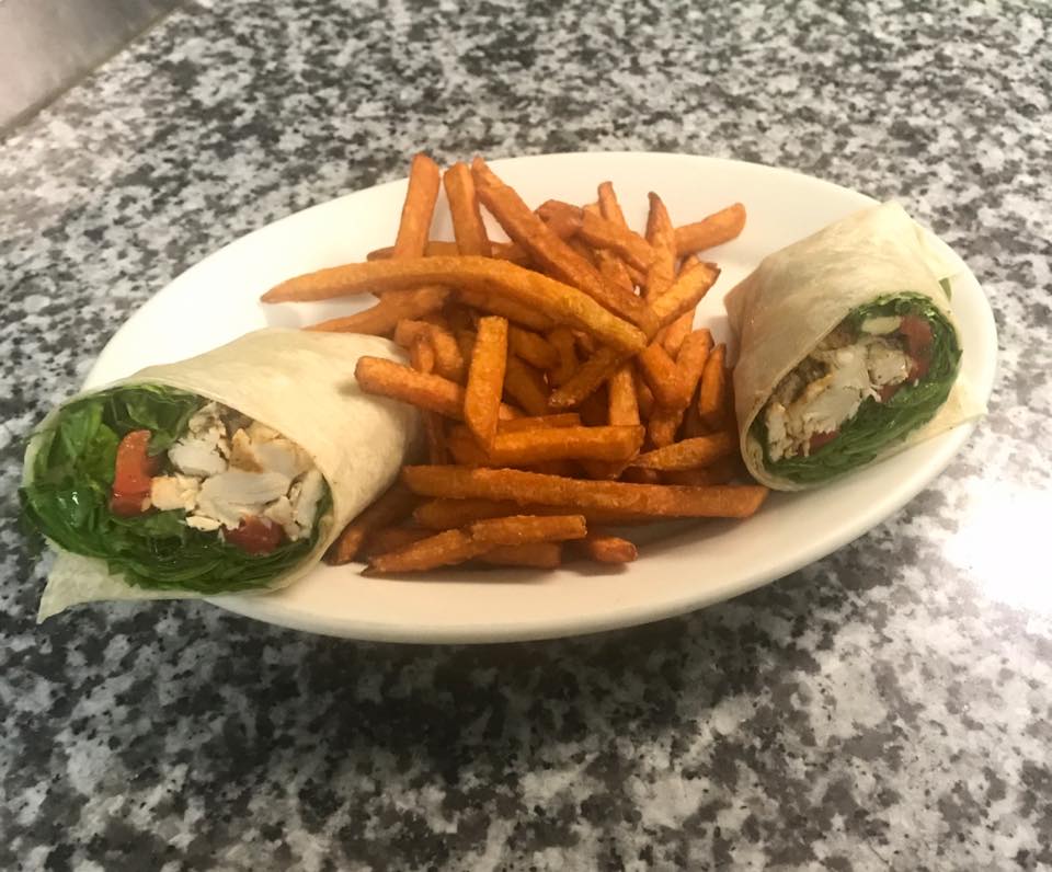 A plate of food with a wrap and french fries on a table.