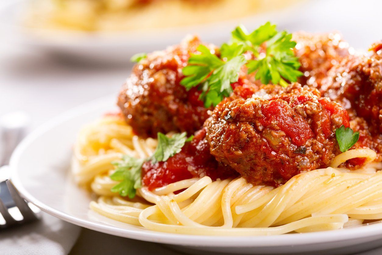 A plate of spaghetti and meatballs with sauce and parsley on a table.