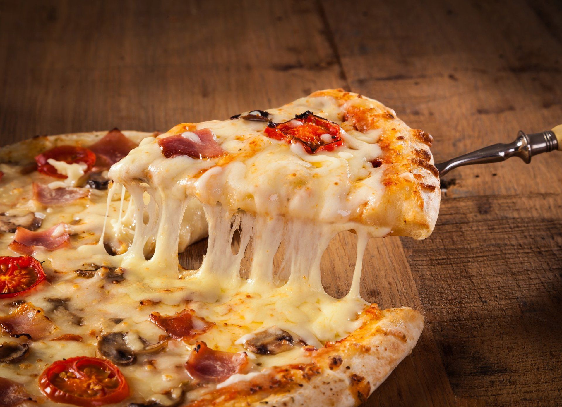 A slice of pizza is being taken out of a pizza on a wooden table.