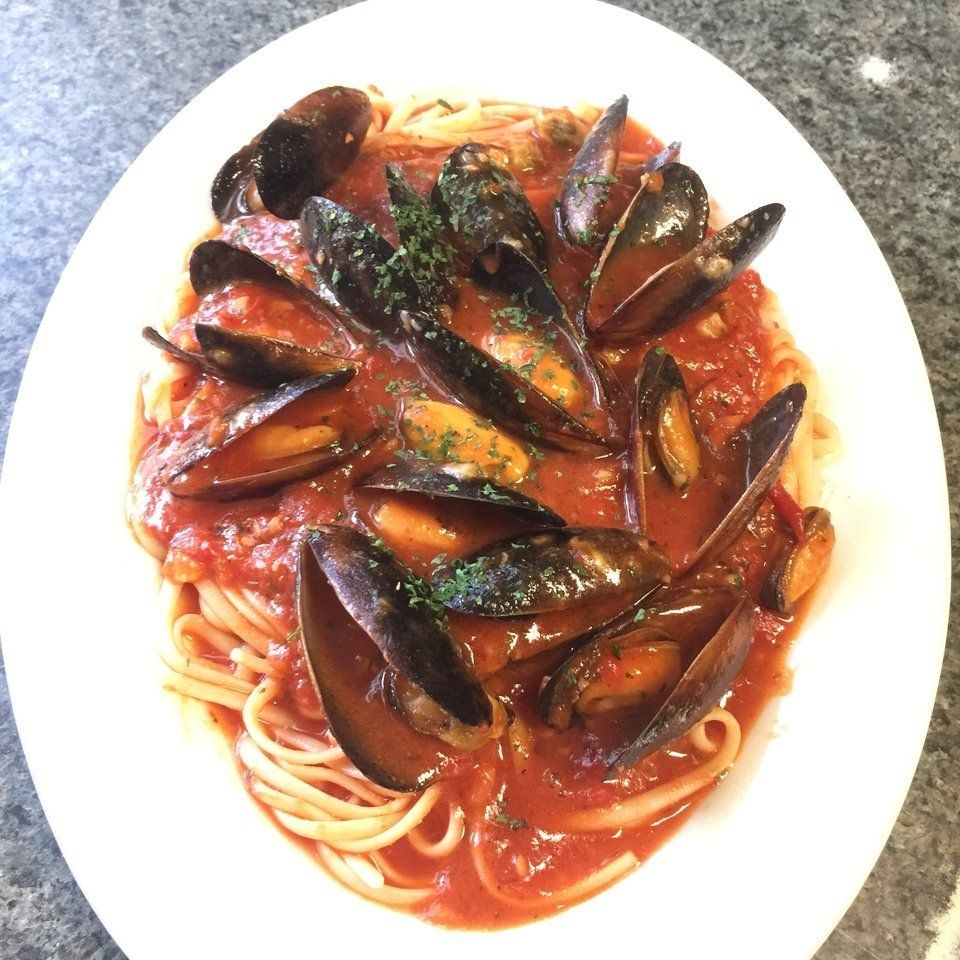 A white plate topped with spaghetti and mussels in tomato sauce