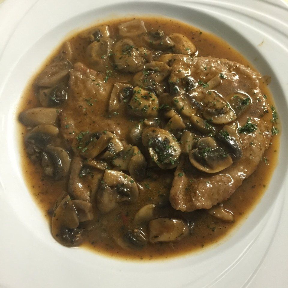 A white plate topped with a stew of meat and mushrooms