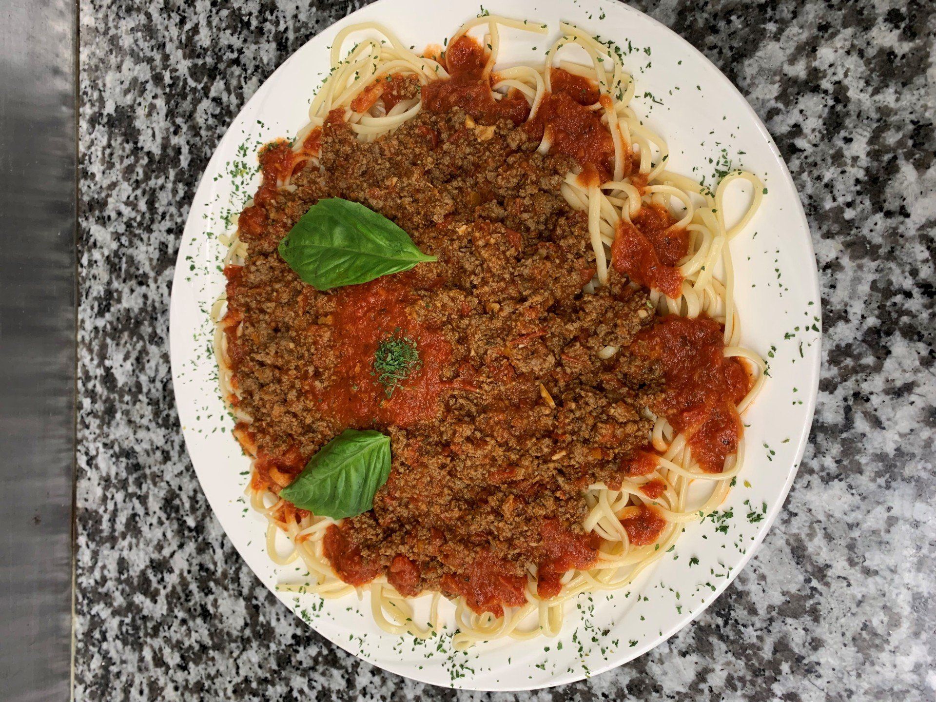 A plate of spaghetti with meat sauce and basil on a table.
