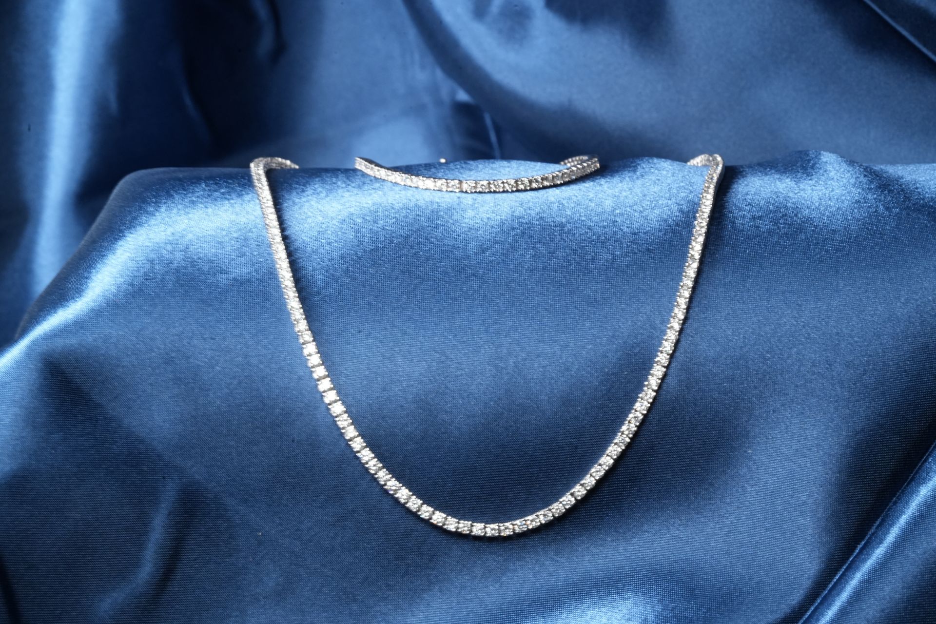 Diamond tennis necklace on shiny blue fabric with matching bracelet 