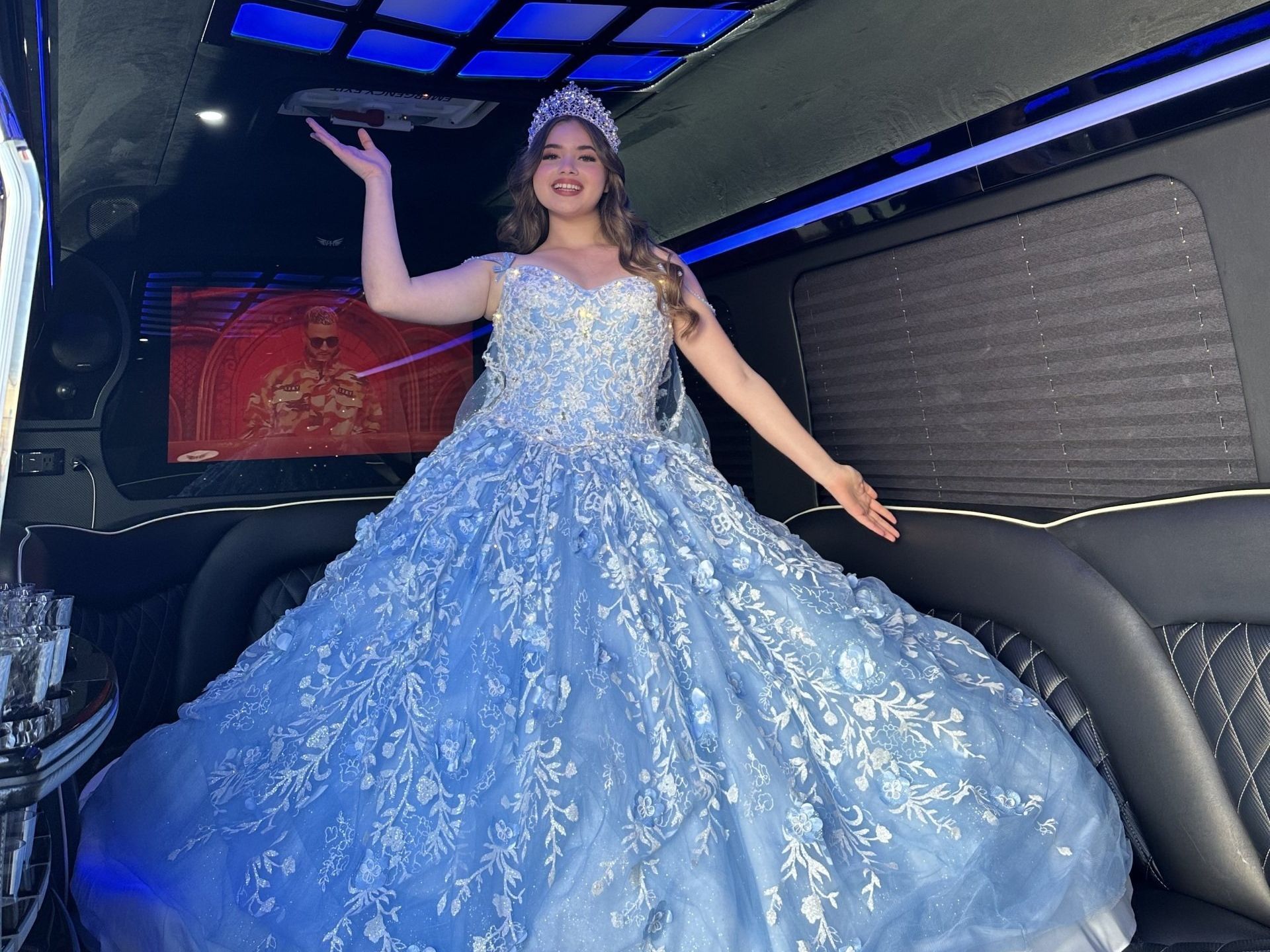 A woman in a blue ball gown is standing in a limousine.